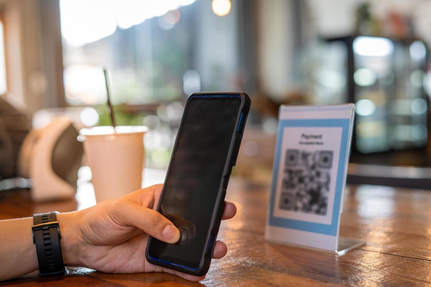 los hombres usan teléfonos para escanear un código qr para seleccionar un menú o escanear para recibir un descuento o pagar comida y bebida dentro de un café. usar el teléfono para transferir dinero o pagar en línea sin concepto de efectivo. foto