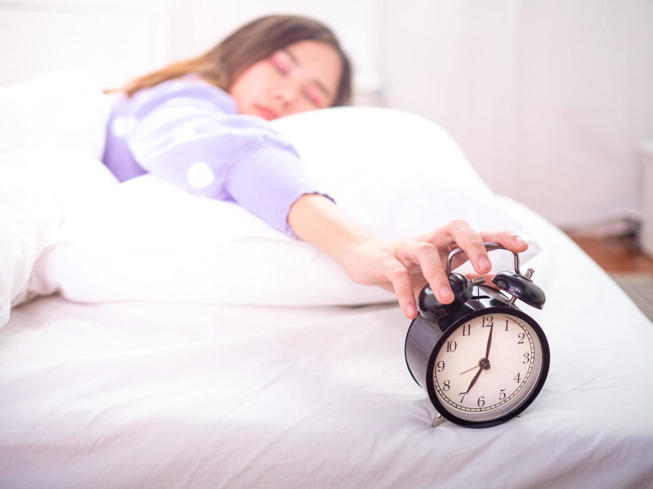 Sleepy girl in bed with eyes closed Reach out to the alarm clock at home. Good morning on a lazy day photo