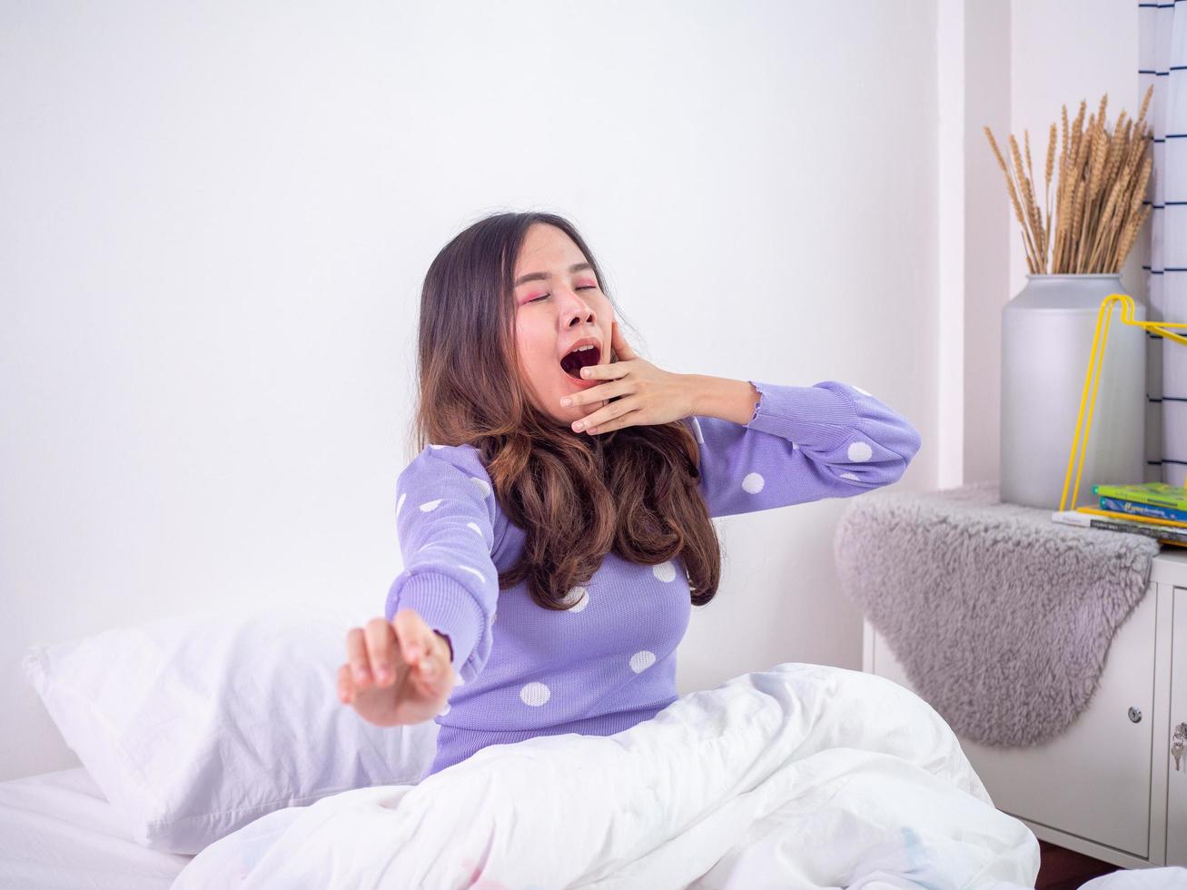 la niña se despierta por la mañana acostada en la cama, todavía con sueño, retorciéndose y bostezando en el dormitorio. mujer perezosa en fin de semana foto