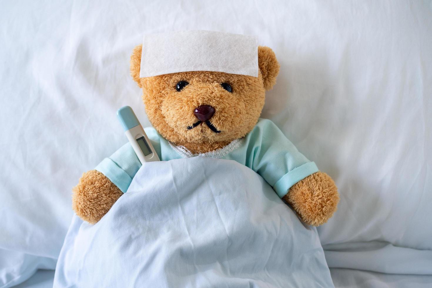 Sick bear is wearing patient clothes. lying in bed with fever, a fever-reducing gel on his forehead and at the temperature temple, put it under the armpit photo