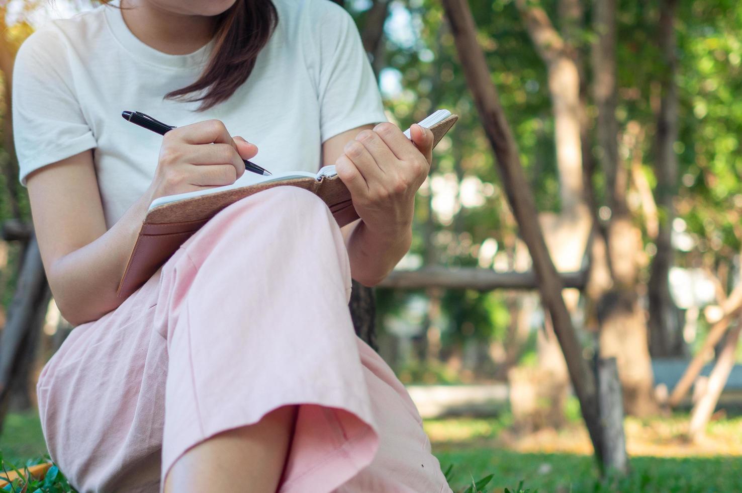 Woman writer sitting  under a tree in the park. Write a book in a shady and quiet atmosphere outside. photo