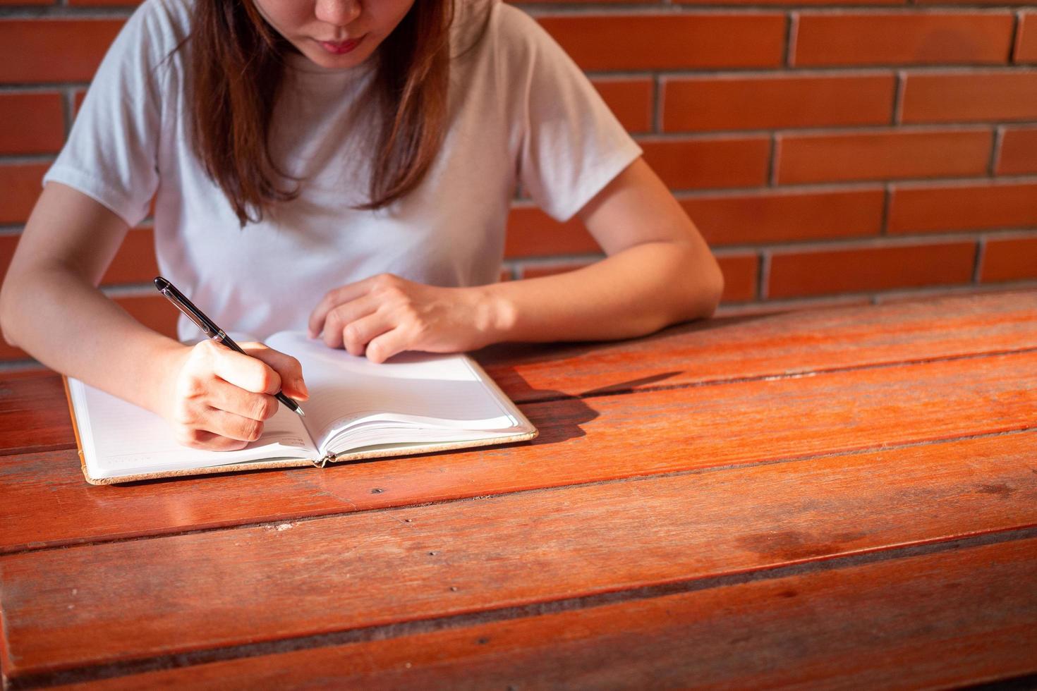 la chica con una camisa blanca sentada en una mesa de madera y escribiendo un libro. hay sol en manos de una mujer joven. conceptos, estudiantes, escritores foto