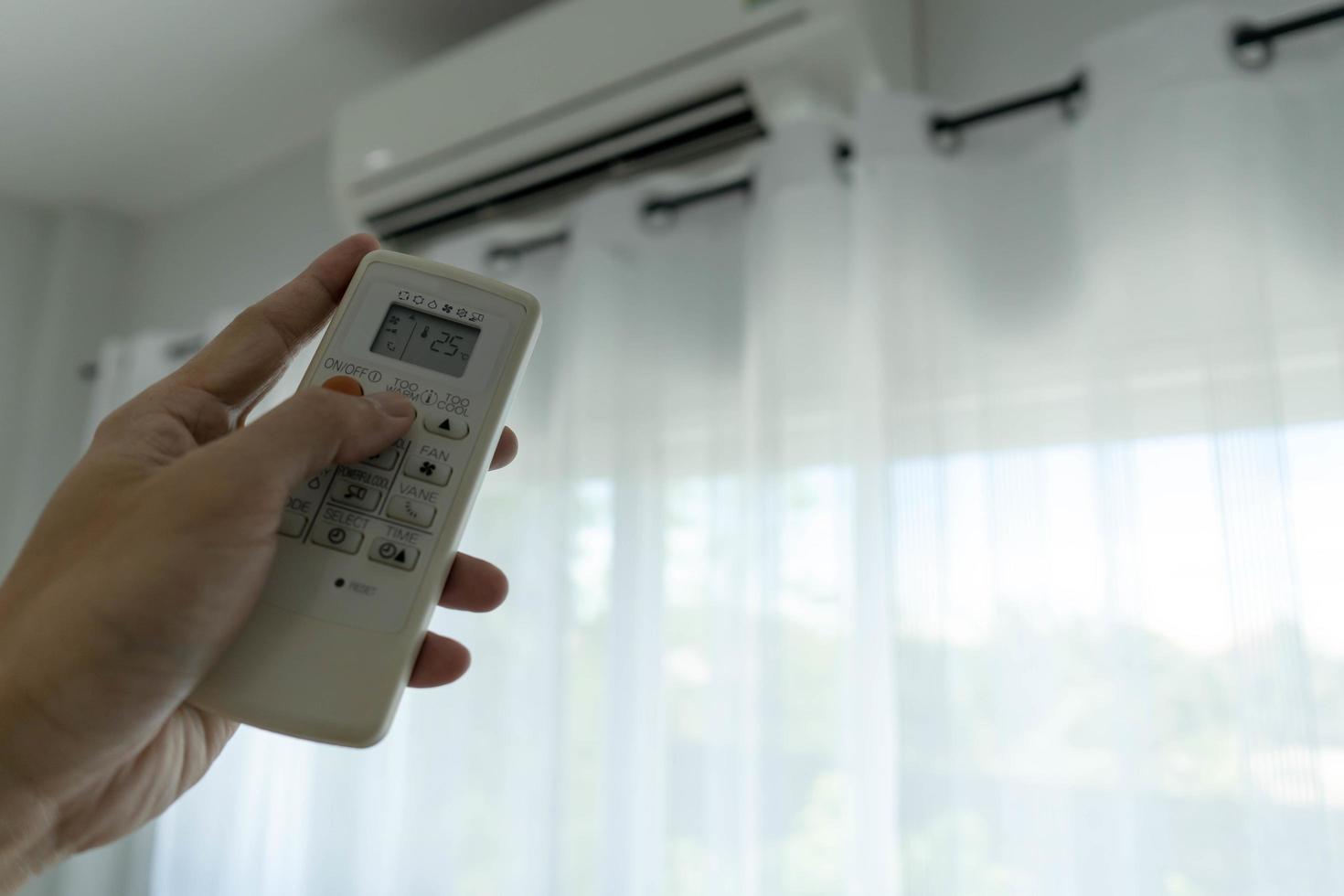 la mano del hombre fuera del acondicionador de aire sujetando el control remoto al sistema de refrigeración después de que no haya nadie en la habitación. Ahorre electricidad, ahorre energía y proteja el medio ambiente. foto