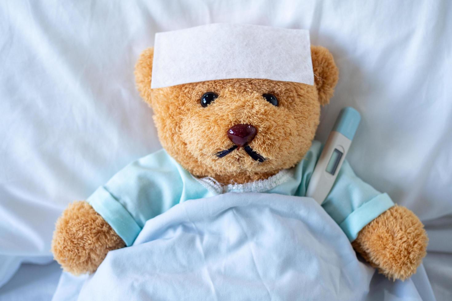 The teddy bear slept with a high fever in the bed. Together with a thermometer. photo