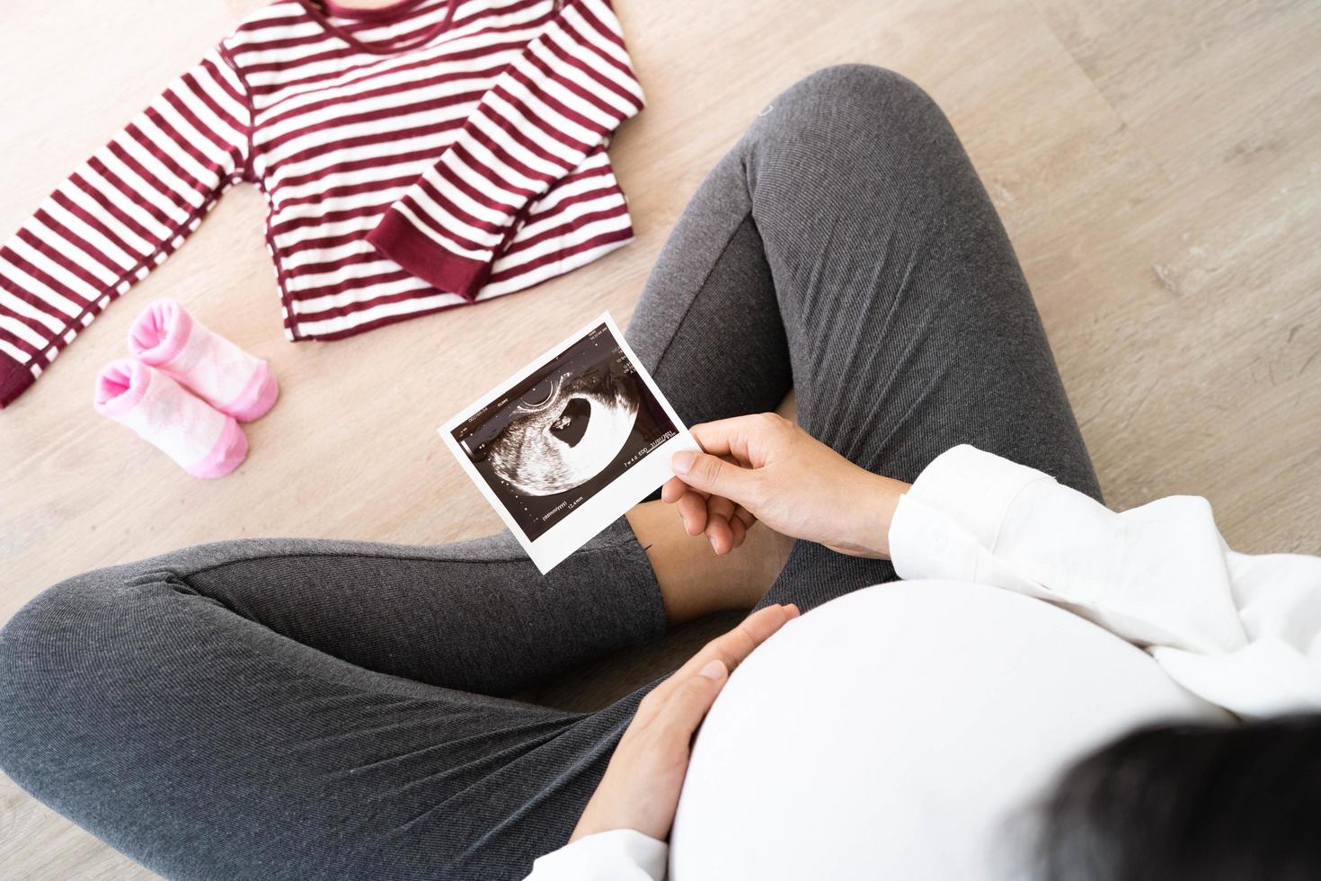 A pregnant woman is looking at an ultrasound photo of fetus. Mother gently touches the baby on stomach.Women are pregnant for 30 weeks. first love in belly and Last term pregnancy