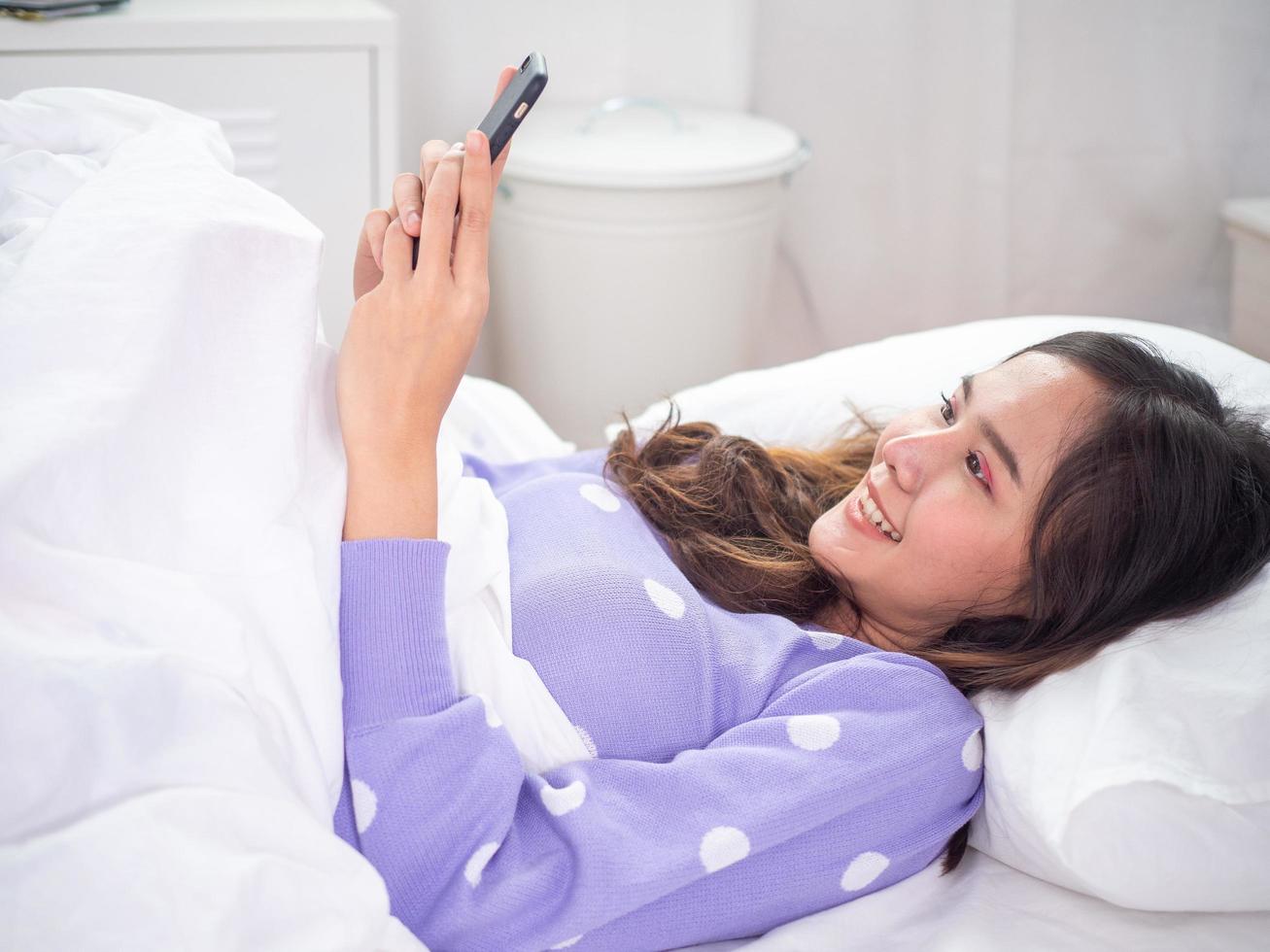 hermosas mujeres tendidas en el teléfono en la cama, usando teléfonos móviles, videoconferencias. utilizar la tecnología para adaptarse a la situación de cuarentena. use teléfonos para personas modernas y en el hogar. foto