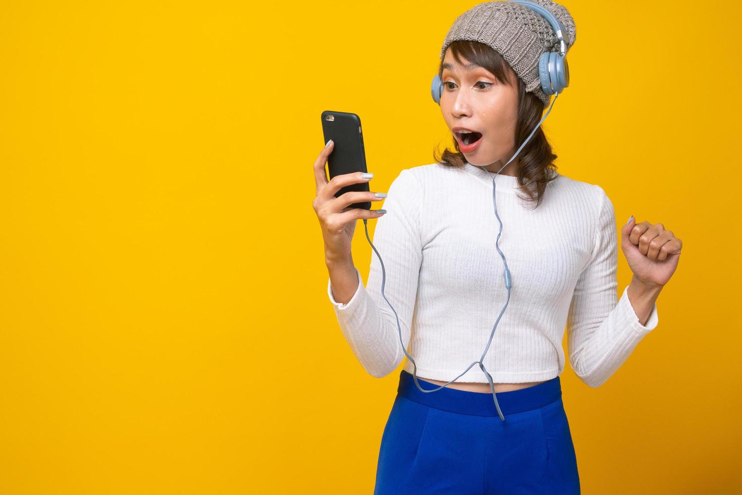 una mujer asiática está haciendo una llamada telefónica y leyendo mensajes telefónicos conmocionada y emocionada. el fondo amarillo brillante. concepto de sorpresa y asombro foto