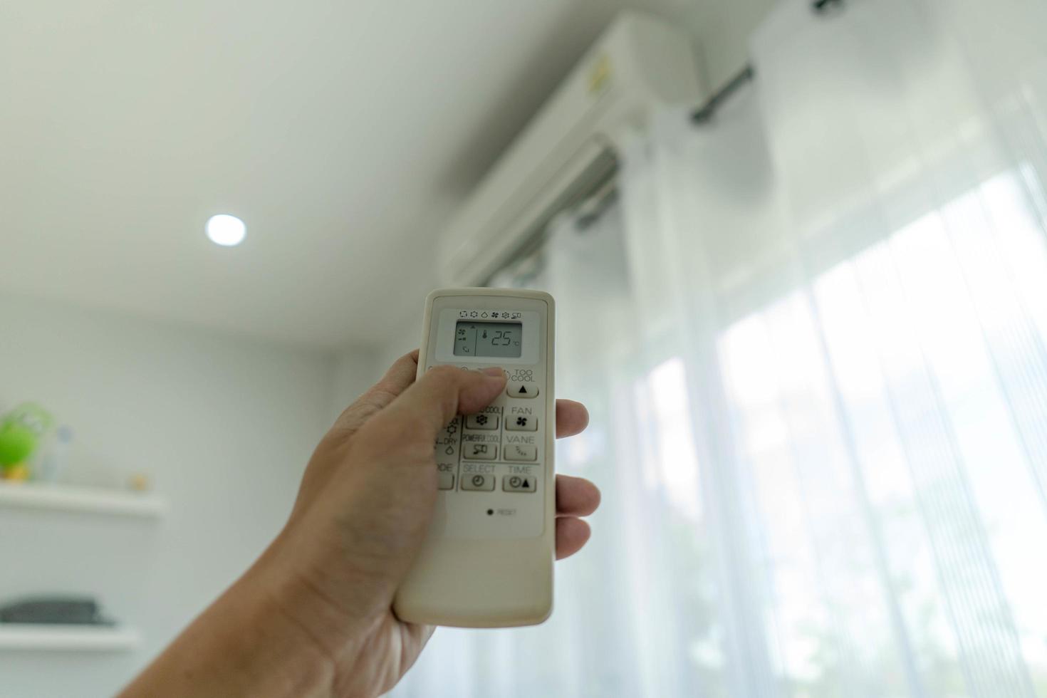 la mano del hombre fuera del acondicionador de aire sujetando el control remoto al sistema de refrigeración después de que no haya nadie en la habitación. Ahorre electricidad, ahorre energía y proteja el medio ambiente. foto