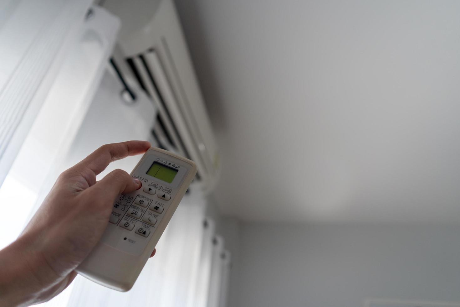 la mano del hombre fuera del acondicionador de aire sujetando el control remoto al sistema de refrigeración después de que no haya nadie en la habitación. Ahorre electricidad, ahorre energía y proteja el medio ambiente. foto