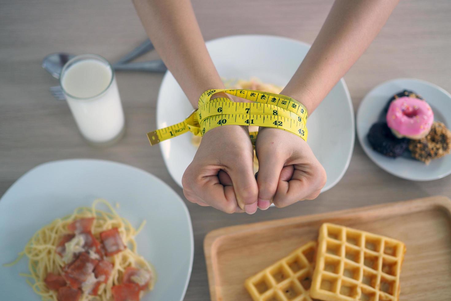 Tape measure around the arms of women. Stop eating trans fats, spaghetti, donuts, waffles and sweets. Lose weight for good health. Top view diet concept photo