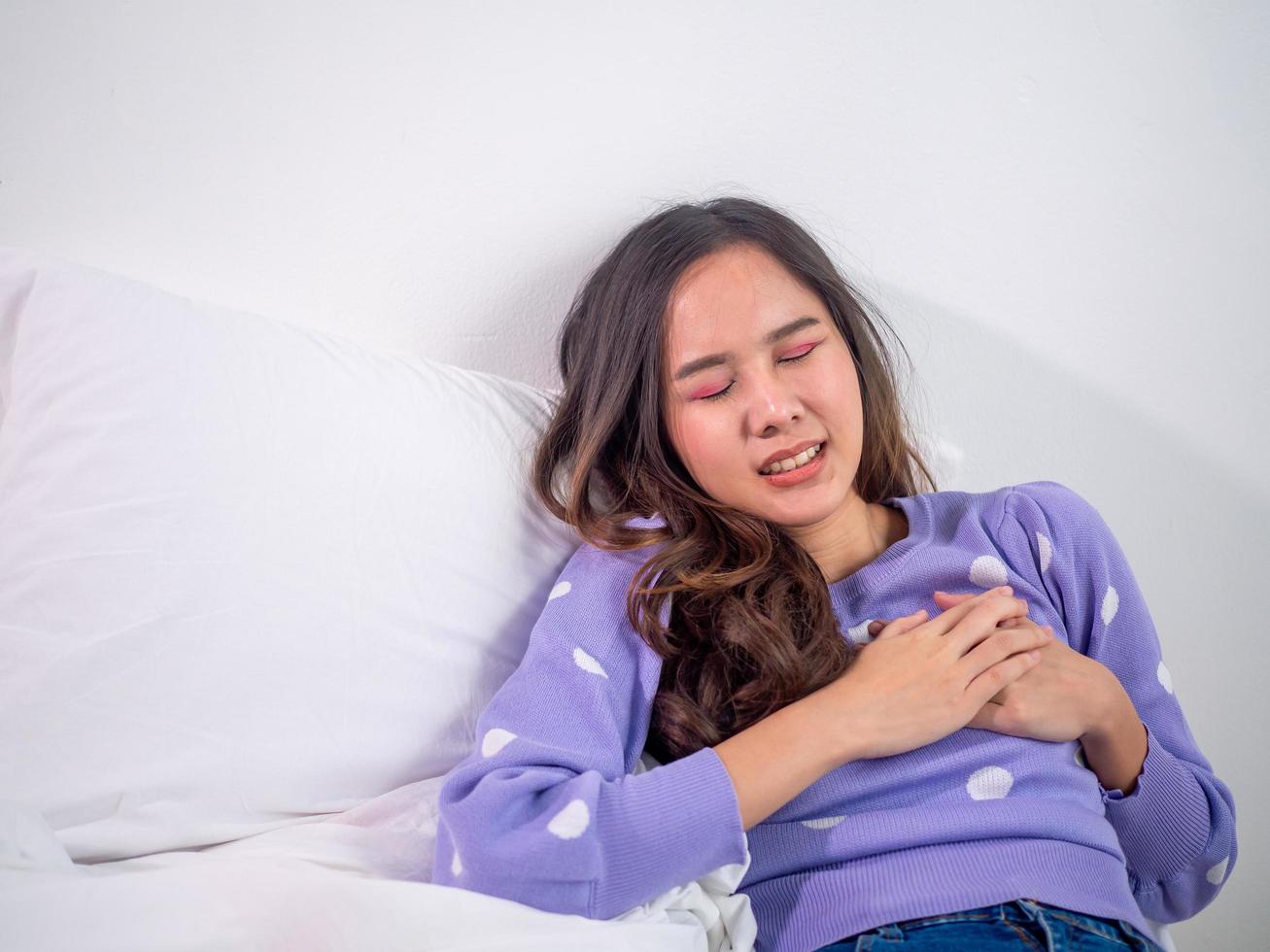 la niña yacía en la cama, usando sus manos para tocar el cofre. dolor cardíaco intenso, ataque cardíaco o calambres, compresiones torácicas dolorosas con expresiones faciales dolorosas foto