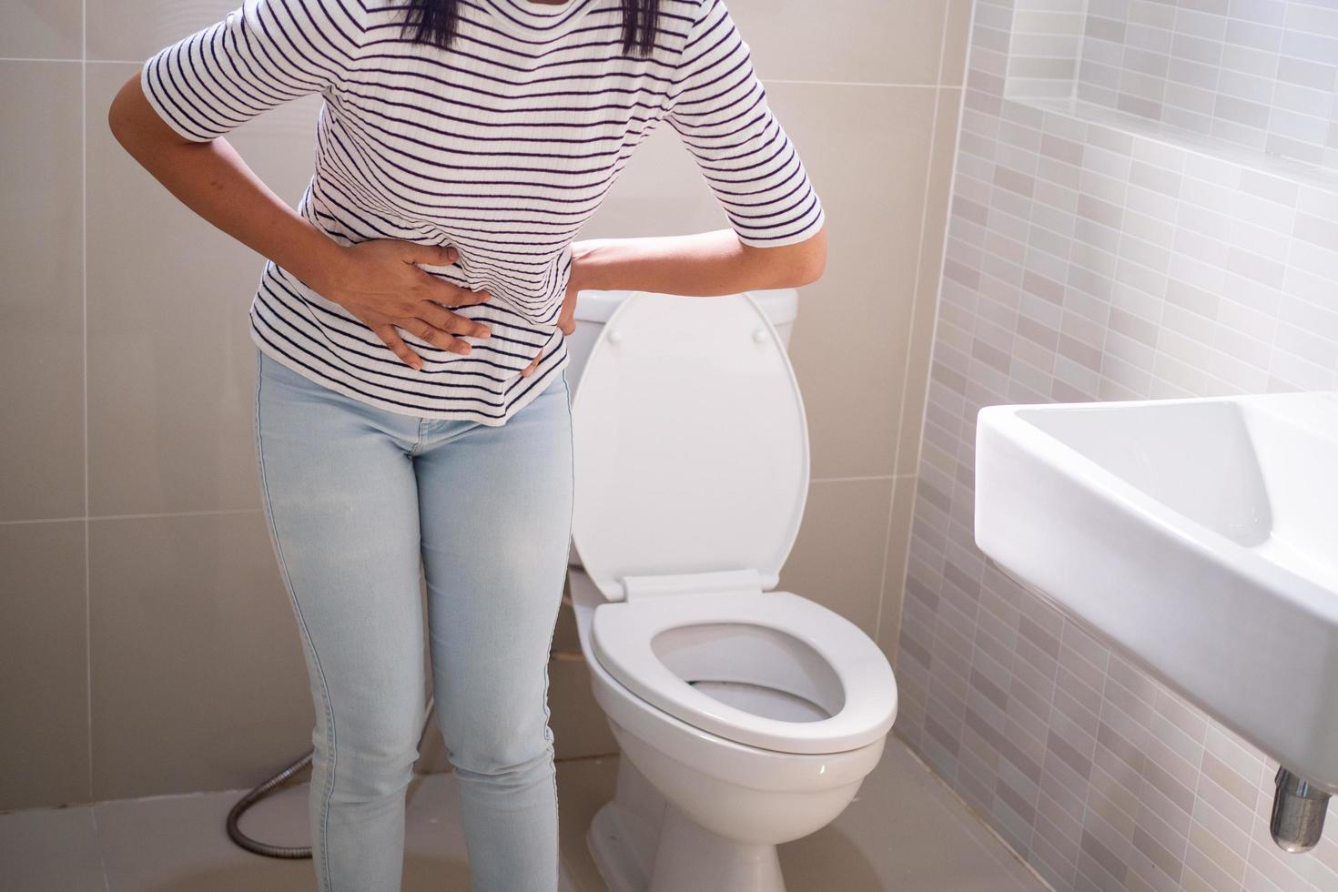 Woman with diarrhea standing in the bathroom, holding her stomach. Severe stomach pain, prepare to sit dung in the bathroom photo