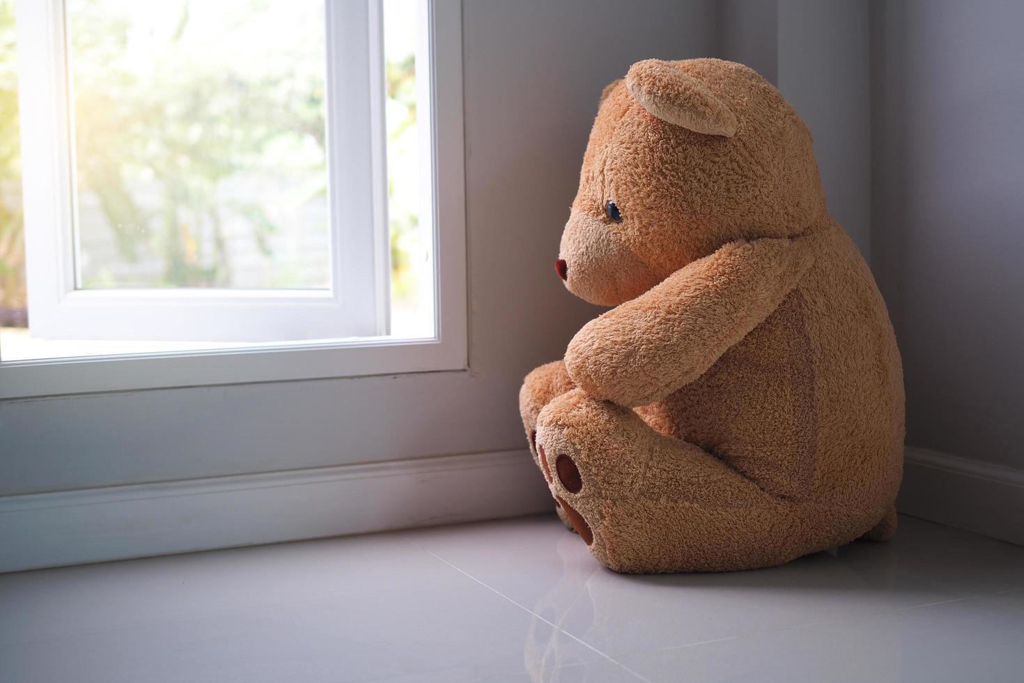 concepto de trastorno depresivo mayor mdd. duelo de los niños. oso de peluche sentado mirando solo la ventana de la casa. parece alguien que está triste, decepcionado, deprimido foto