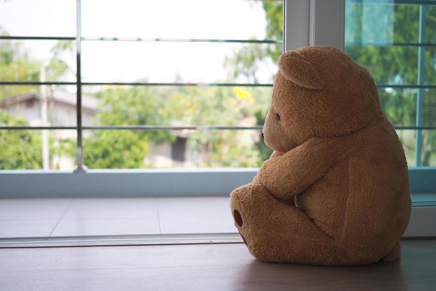 concepto de trastorno depresivo mayor mdd. duelo de los niños. oso de peluche sentado mirando solo la ventana de la casa. parece alguien que está triste, decepcionado, deprimido foto