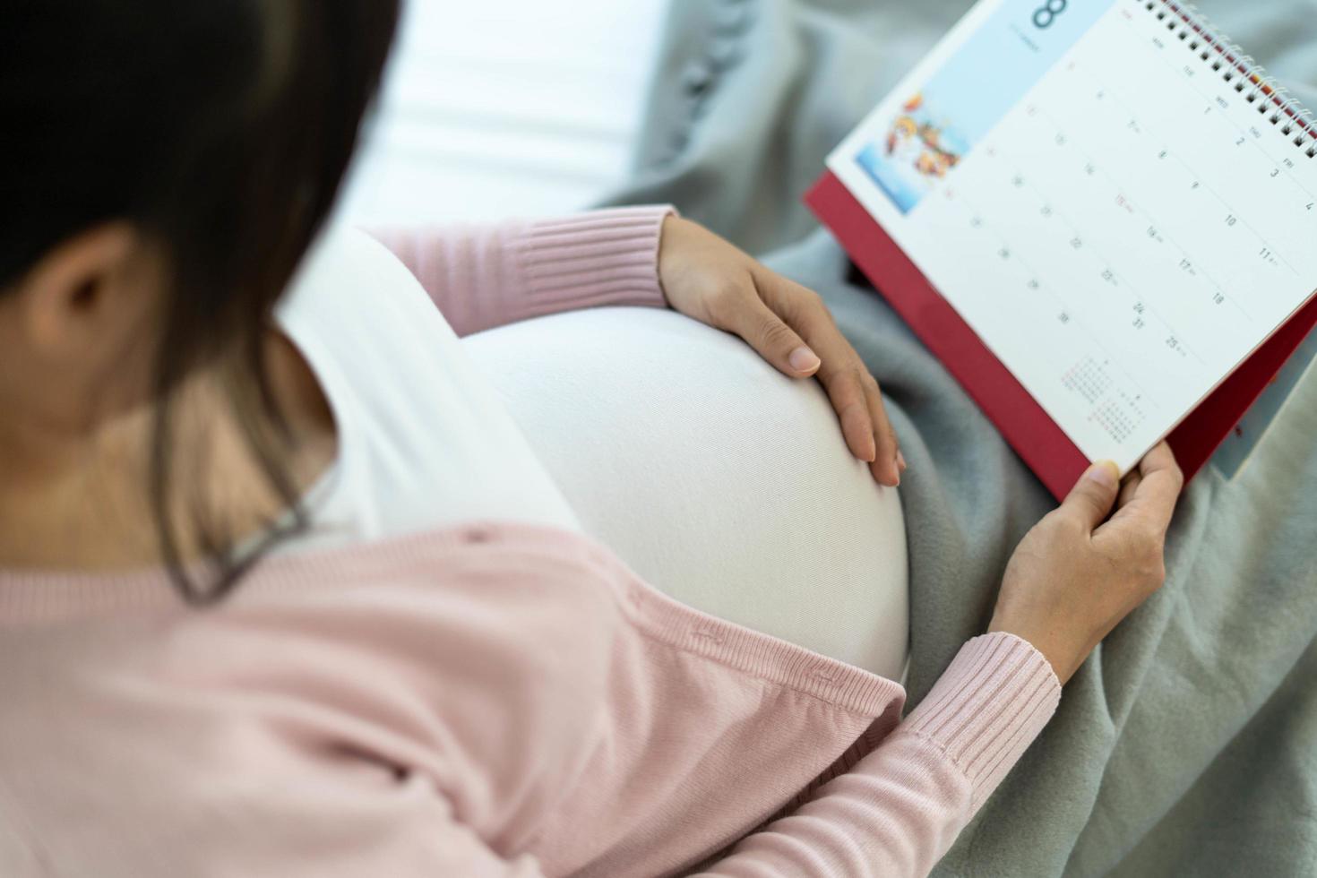 A pregnant woman touches her belly with her hand and looks at the date of birth on the calendar. photo