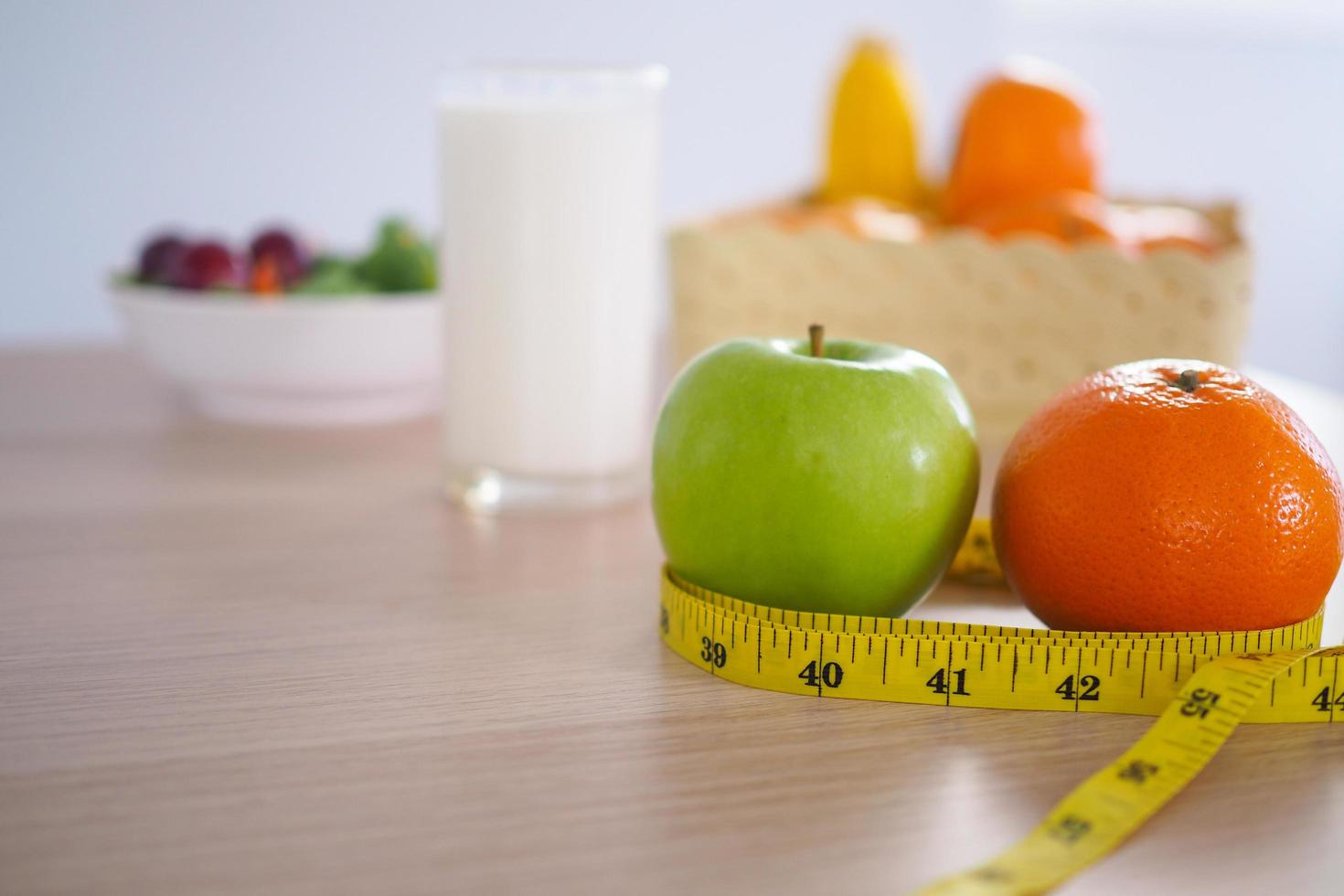 cinta métrica alrededor de la manzana verde. a continuación hay ensalada de leche y verduras en la mesa de madera. comer para una buena salud y pérdida de peso. concepto de dieta foto