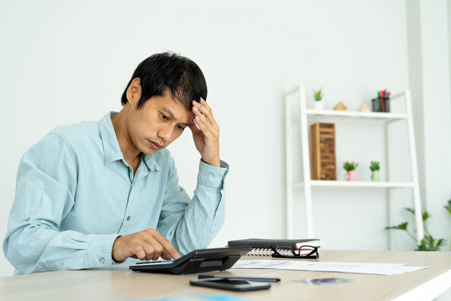 Asian businessmen are pressing a calculator to calculate costs and profits and losses. Men stressed by monthly debt problems Debt concept photo