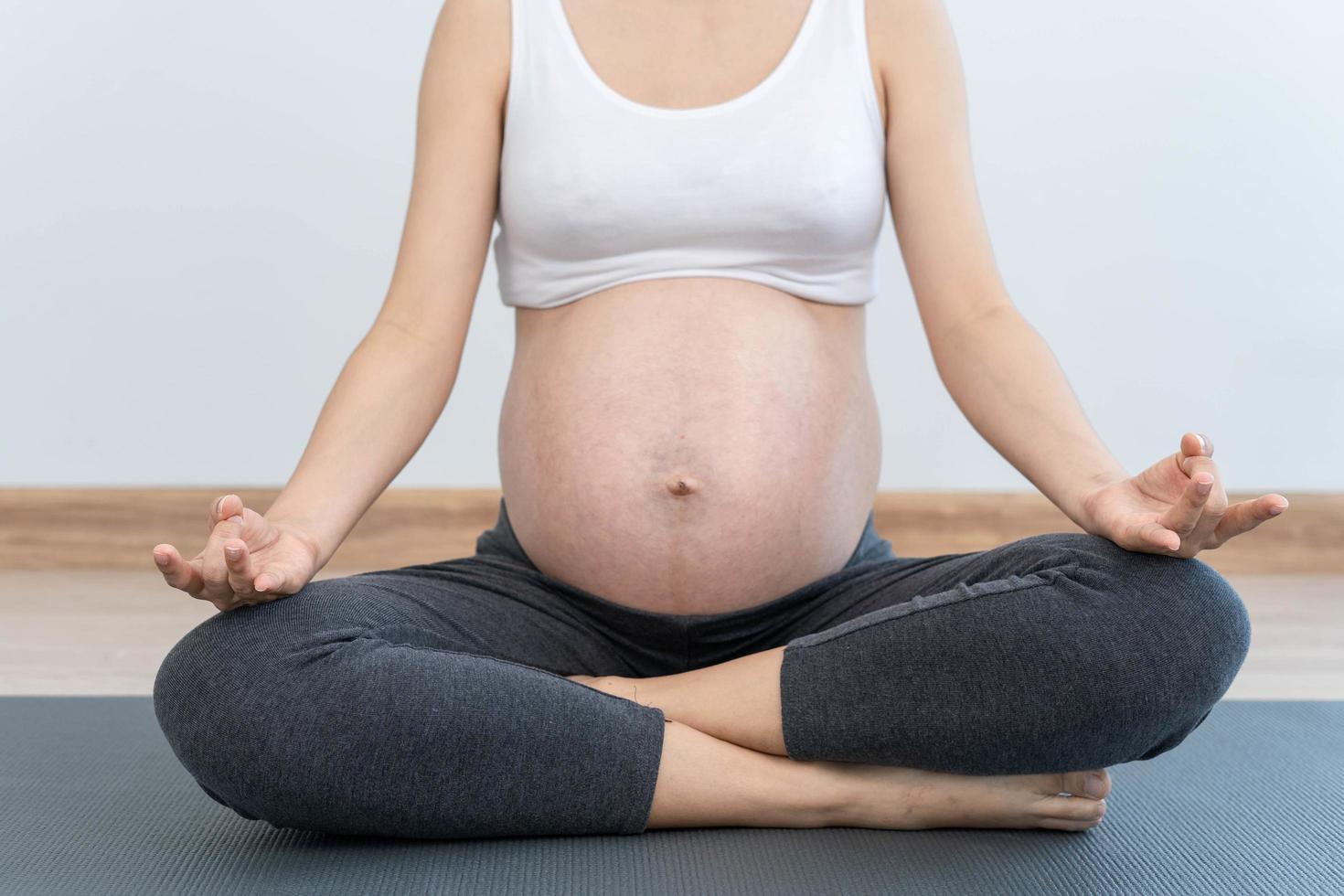 mujer pragnante practicando yoga en casa. hermosa joven haciendo ejercicios en casa. equilibrio, meditación, relajación, concepto de estilo de vida saludable foto