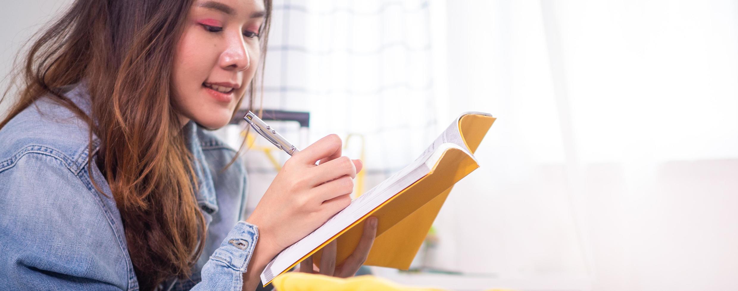 The girl writing notes with a pen in a yellow booklet Happily being in the room at home. photo
