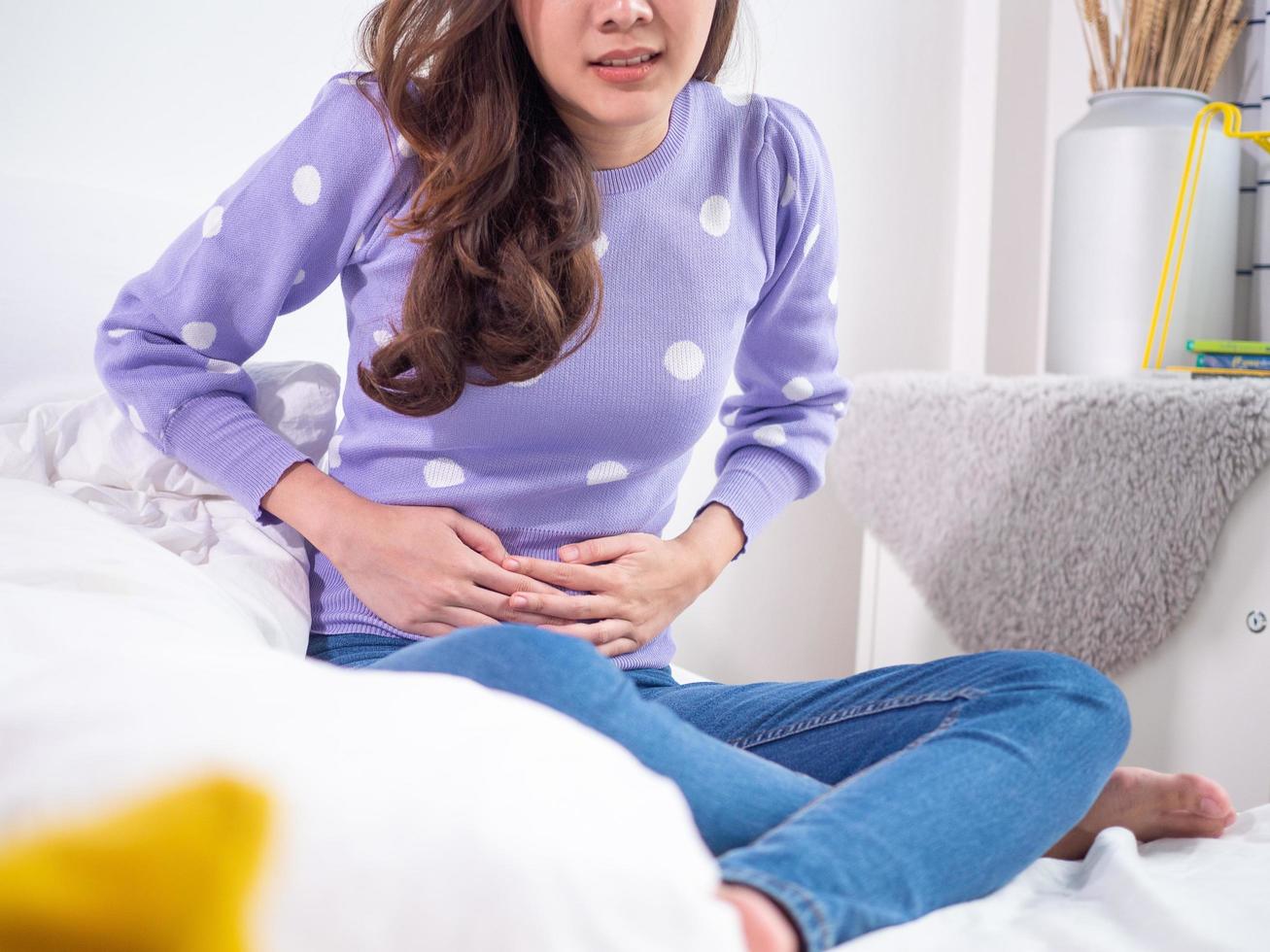 mujer con dolor de estómago en la cara, sintiéndose herida, torturada, usando ambas manos para presionar su estómago. la causa puede ser de muchas enfermedades. concepto de menstruación foto