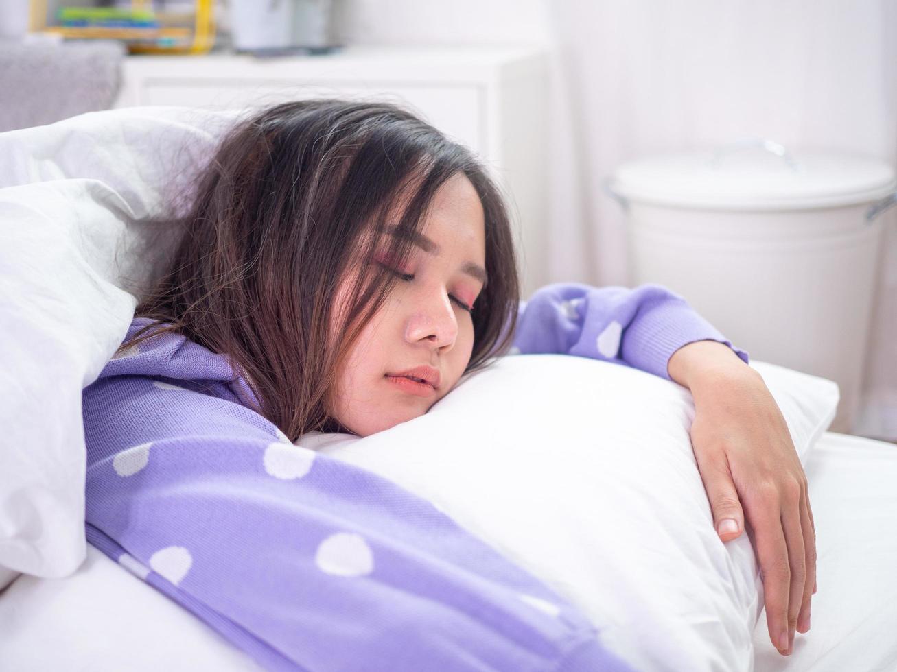 una hermosa mujer asiática está durmiendo y abrazando una almohada en vacaciones. mujer perezosa despierta o despierta tarde concepto foto