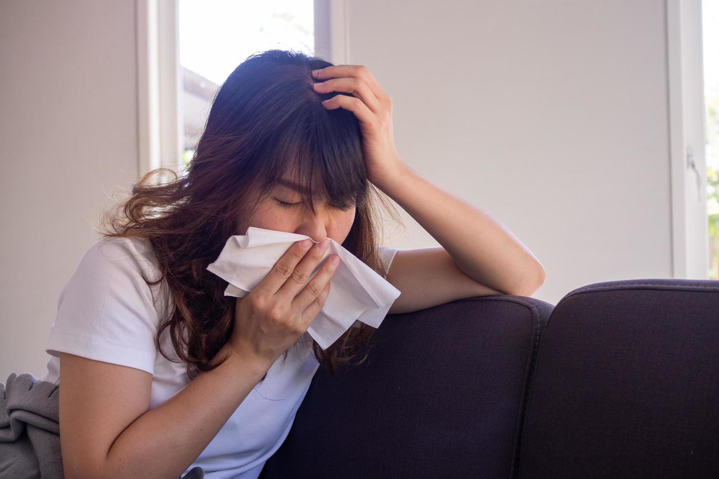 Asian woman sitting on the sofa inside the house having a fever, having a mouth cloth after covering the mouth after preventing spreading COVID-19 is currently spreading around the world photo