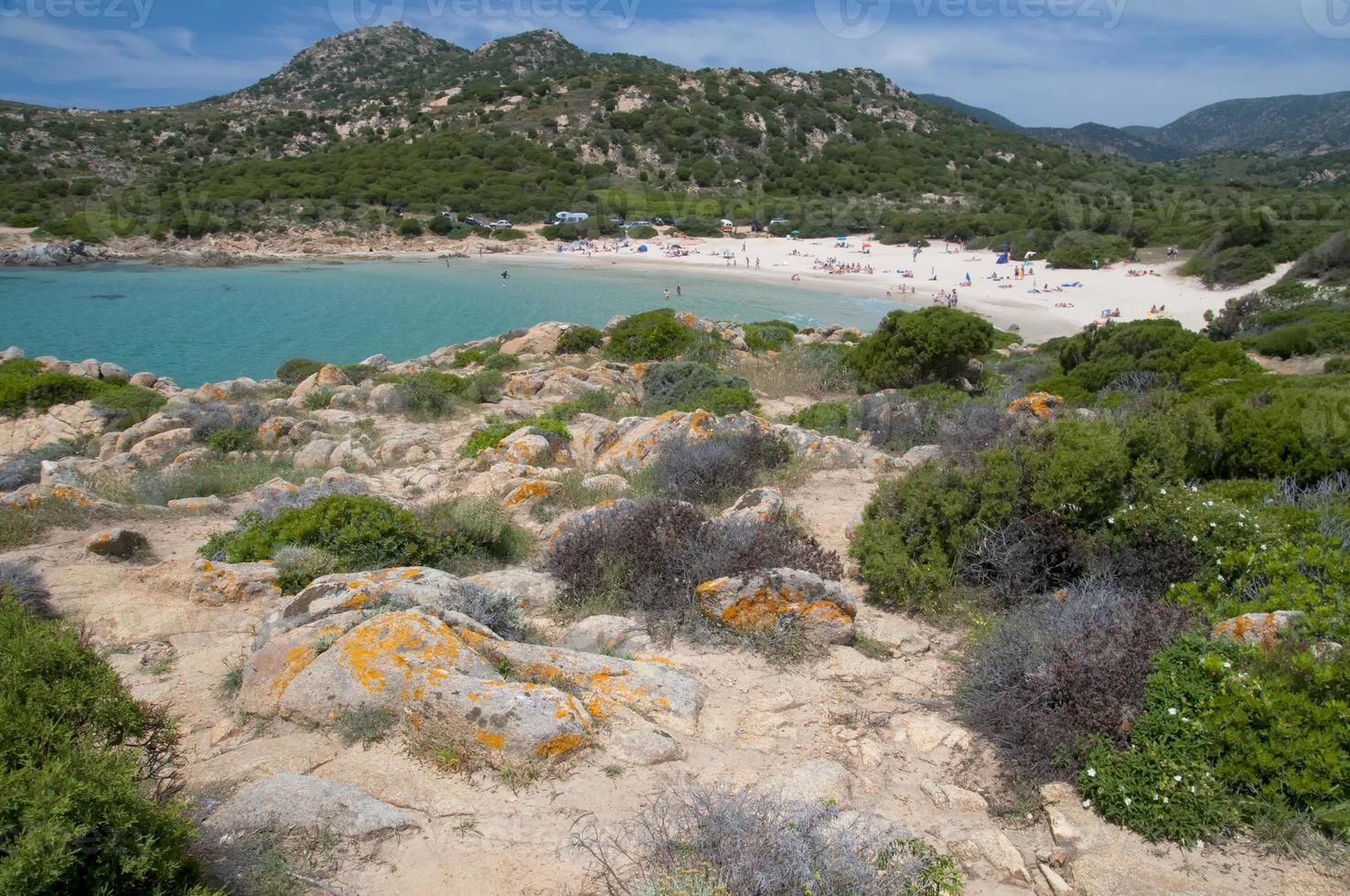 A turquoise blue sea and white sand beach with rocks in Sardinia Italy photo