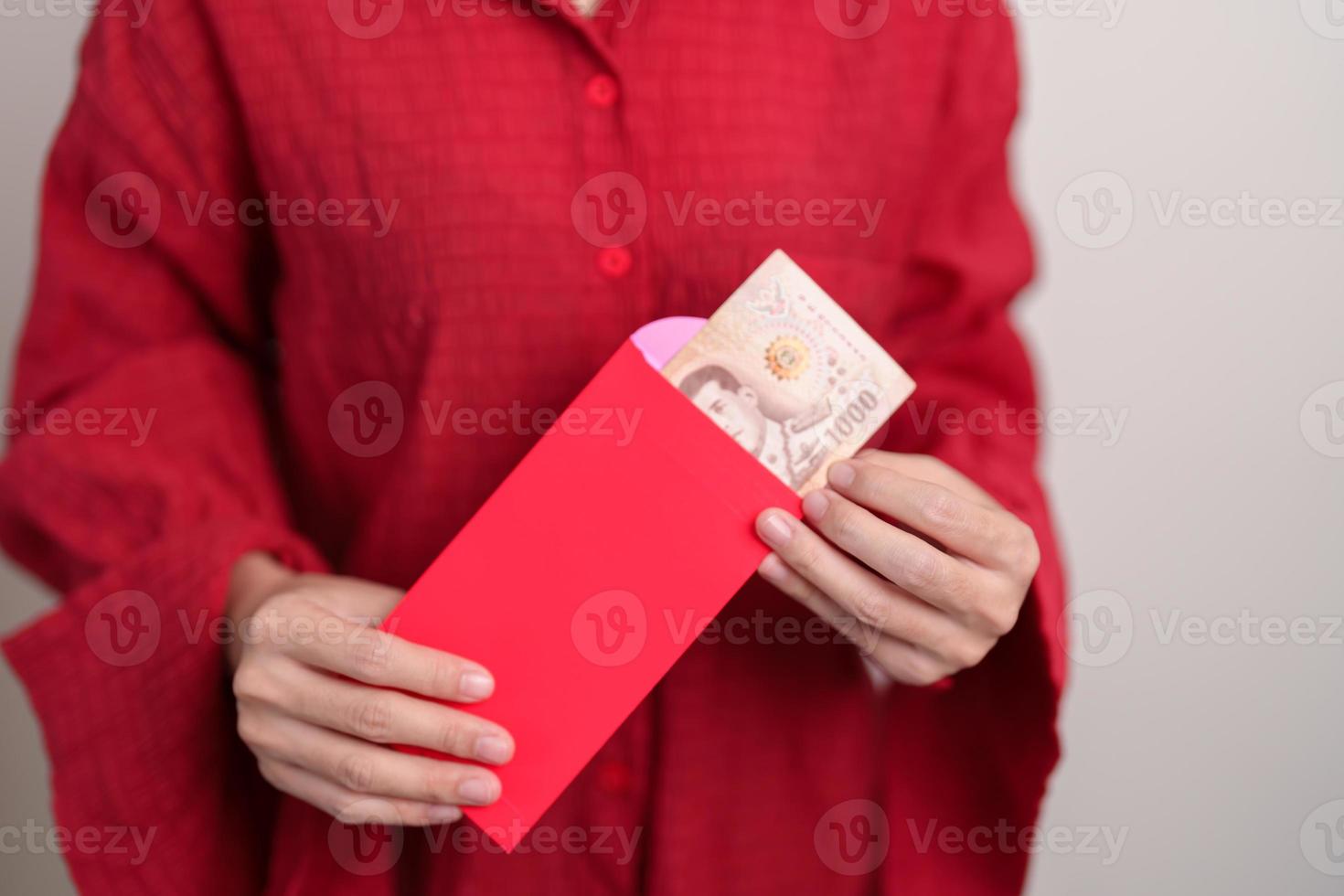 mujer sosteniendo un sobre rojo chino con regalo de dinero en baht tailandés para felices vacaciones de año nuevo lunar foto