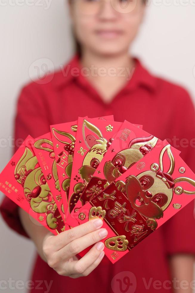 mujer sosteniendo un sobre rojo chino con conejo dorado y palabra de bendición, regalo de dinero para felices vacaciones de año nuevo lunar. frase china significa felicidad, salud, suerte y riqueza foto