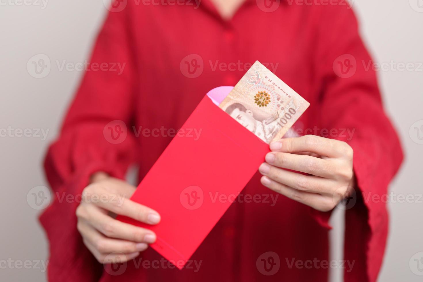 mujer sosteniendo un sobre rojo chino con regalo de dinero en baht tailandés para felices vacaciones de año nuevo lunar foto