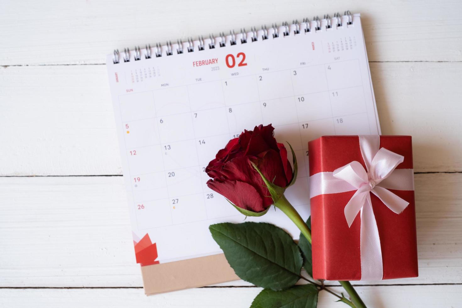 rosa roja y caja de regalo roja en el calendario aislado sobre fondo blanco de madera con. concepto de día de san valentín. planificación programación agenda, evento, organizador día de san valentín. endecha plana, vista superior. foto