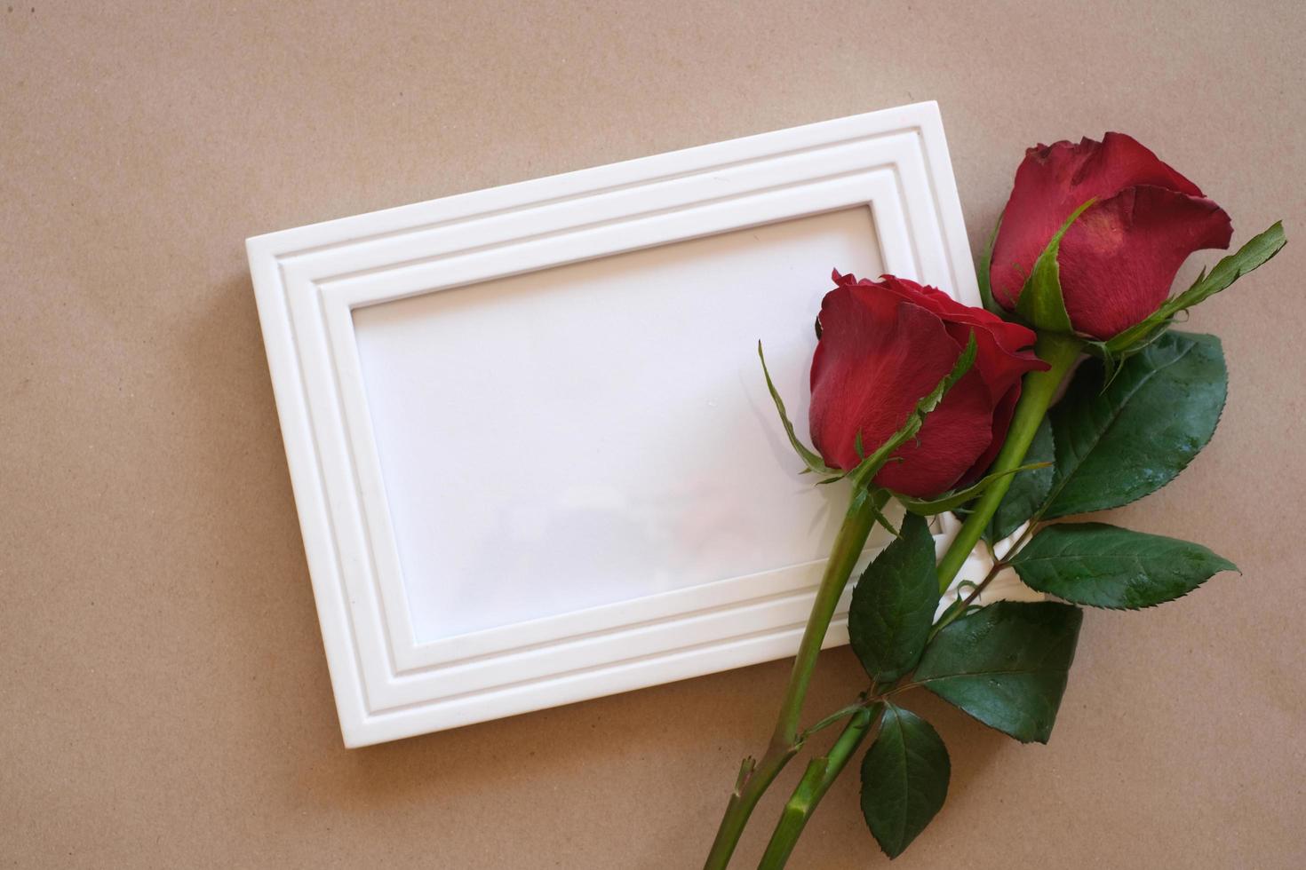 vista superior de rosa roja y corazón rojo sobre un marco de fotos en blanco aislado sobre fondo marrón. concepto de día de san valentín, boda, cumpleaños y ocasiones especiales. endecha plana, vista superior.