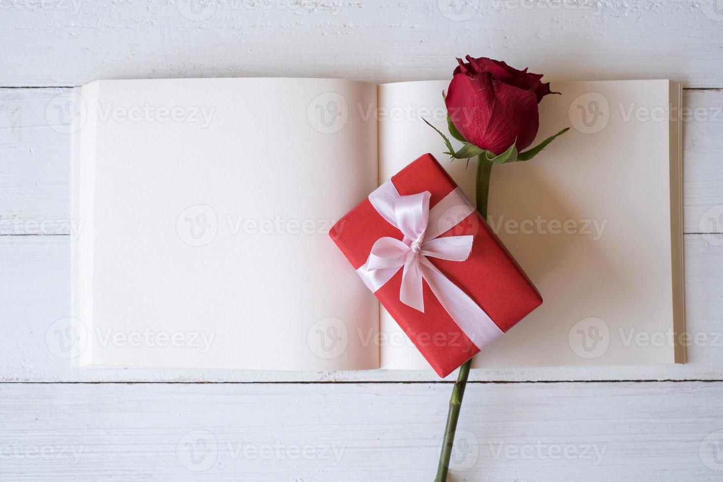 Blank notebook with red roses and red gift box on wooden table. Copy space for your text. Valentine's day, wedding, birthday and special occasion concept. Copy space for text. Top view, Flat lay. photo