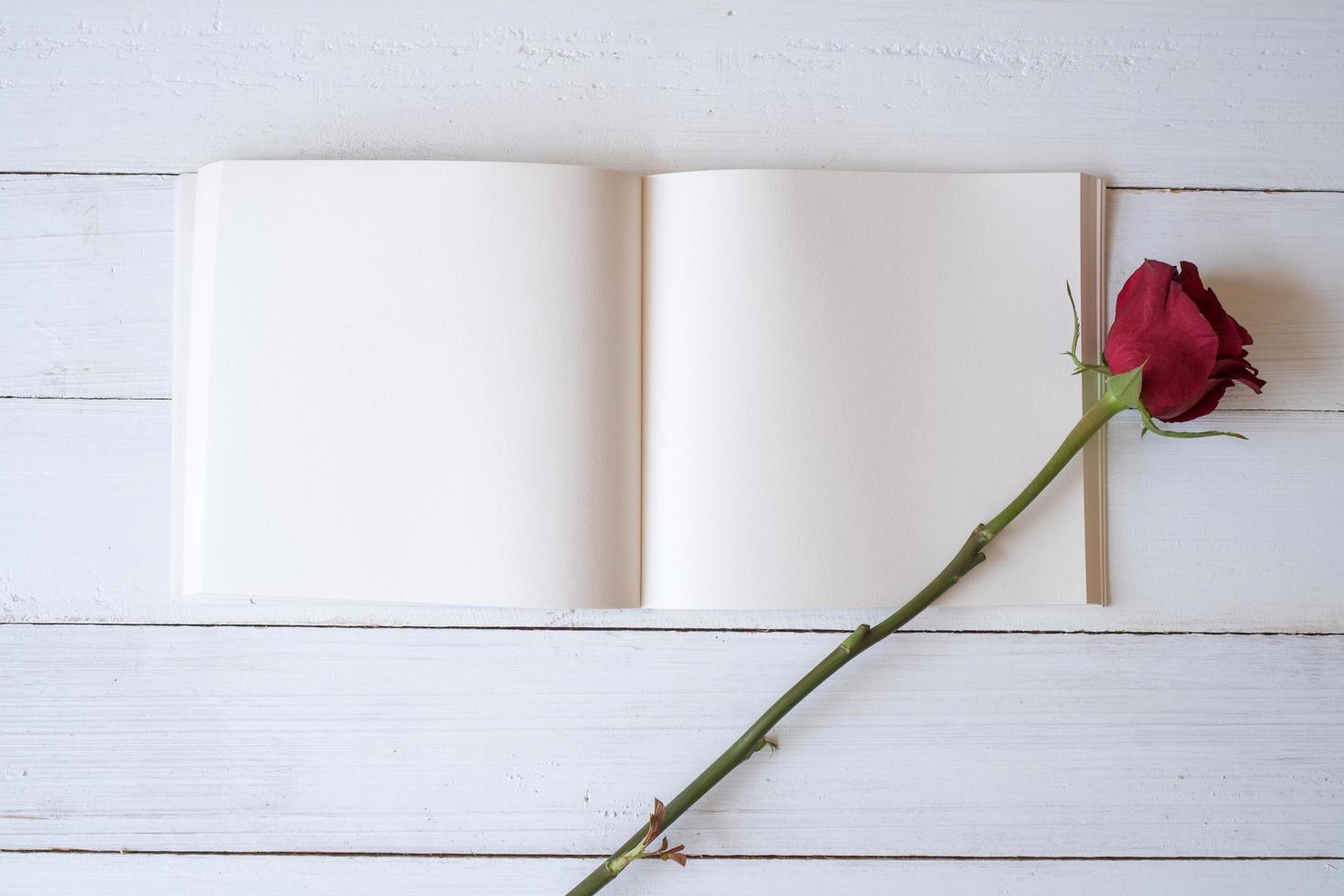 Blank notebook with red roses on wooden table. Copy space for your text. Valentine's day, wedding, birthday and special occasion concept. Copy space for text. Top view, Flat lay. photo