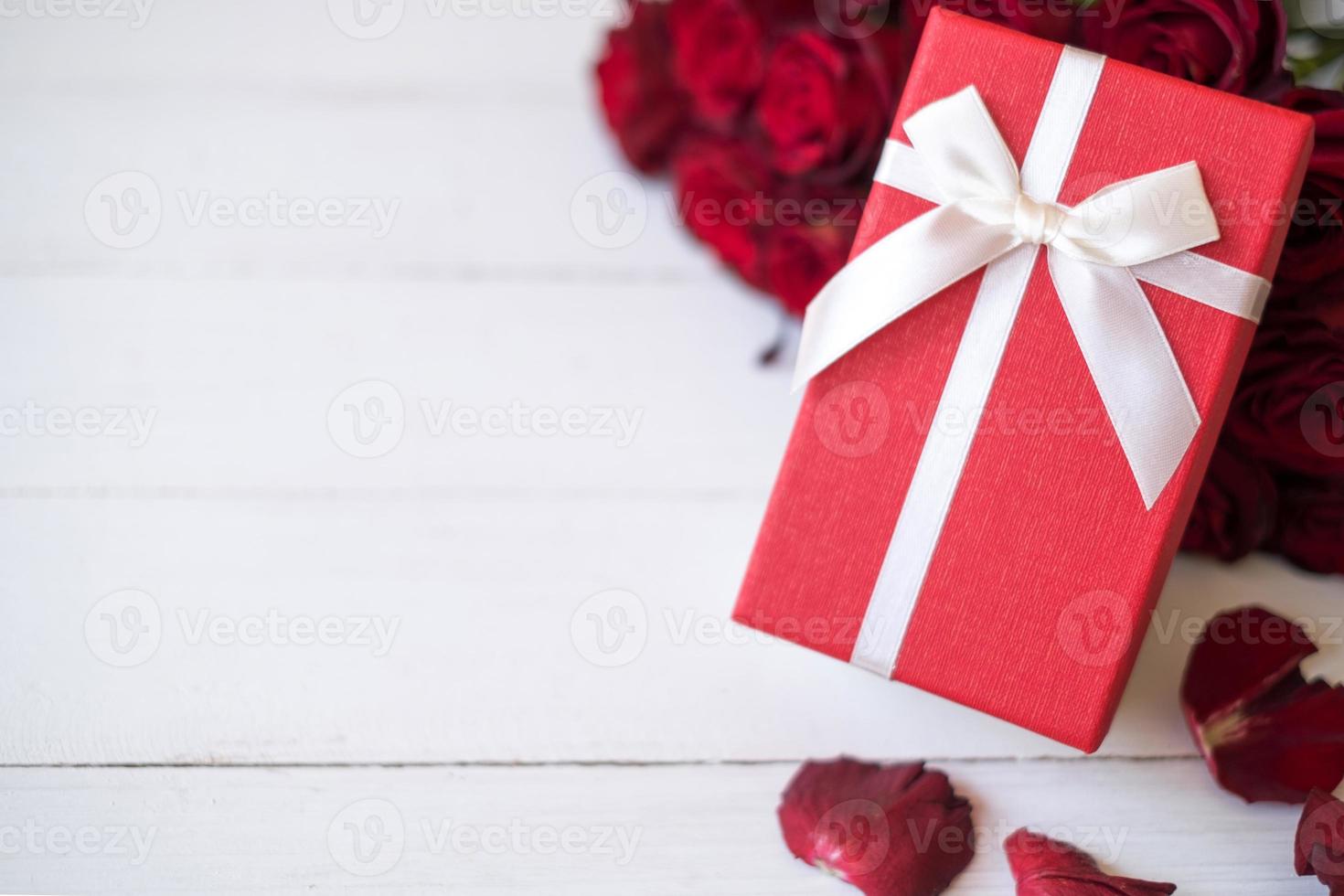 Close up red gift box with bunch of rosy roses blurred background. Valentine's day, wedding, birthday and special occasion concept. Copy space for text. photo
