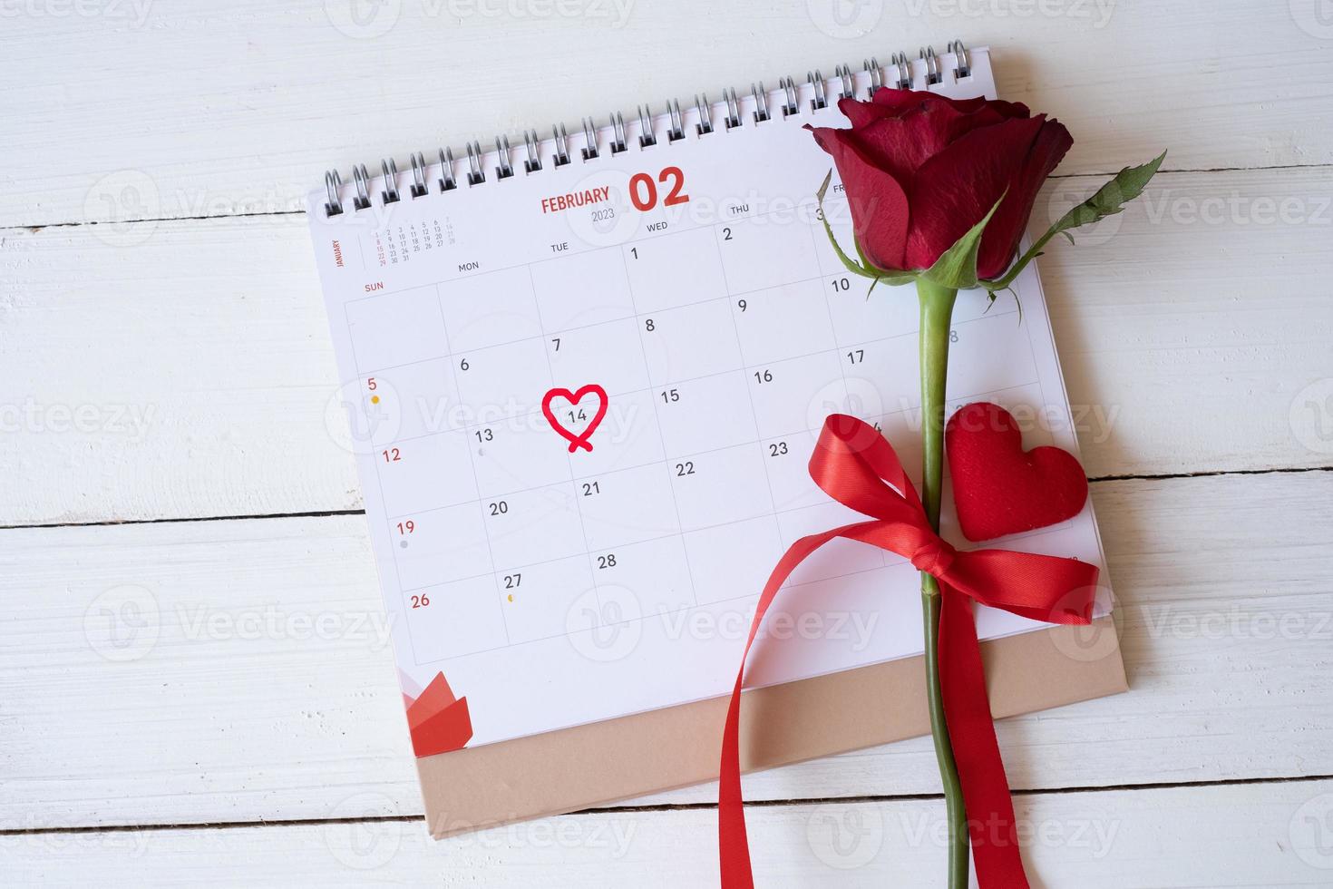 Red rose and a heart on calendar isolated on white wooden background with. Valentine's day concept. Planning scheduling agenda, Event, organiser valentines day. Flat lay, top view. photo