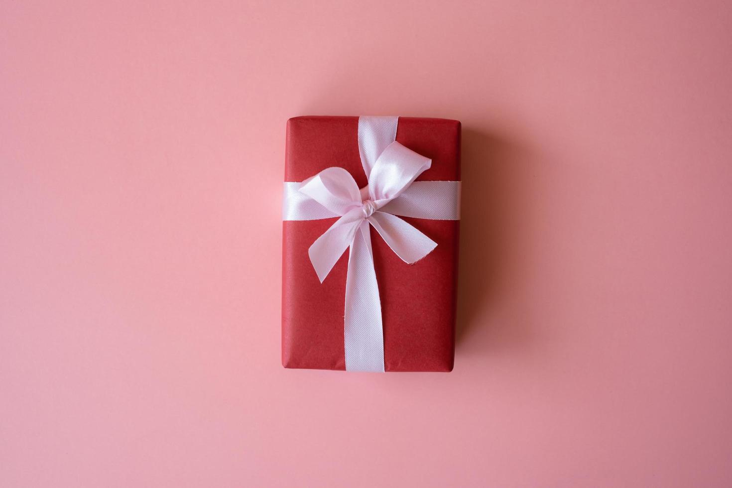 Red gift box with ribbon isolated on pink background for giving in holidays with copy space for text. Holidays, present, giving concept. New year day, Christmas day, Chinese New Year day, Birthday. photo