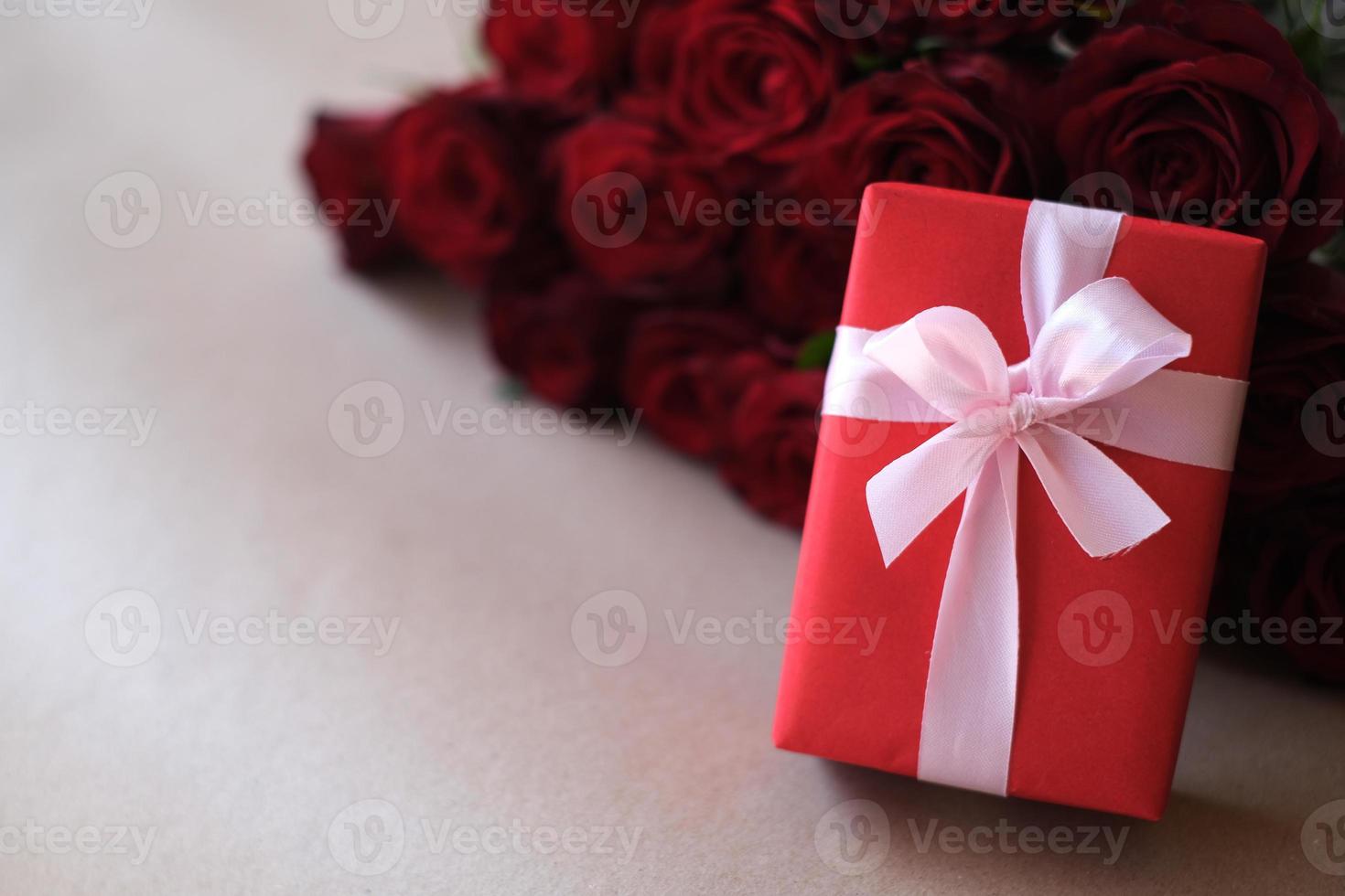 Close up red gift box with bunch of rosy roses blurred background. Valentine's day, wedding, birthday and special occasion concept. Copy space for text. photo
