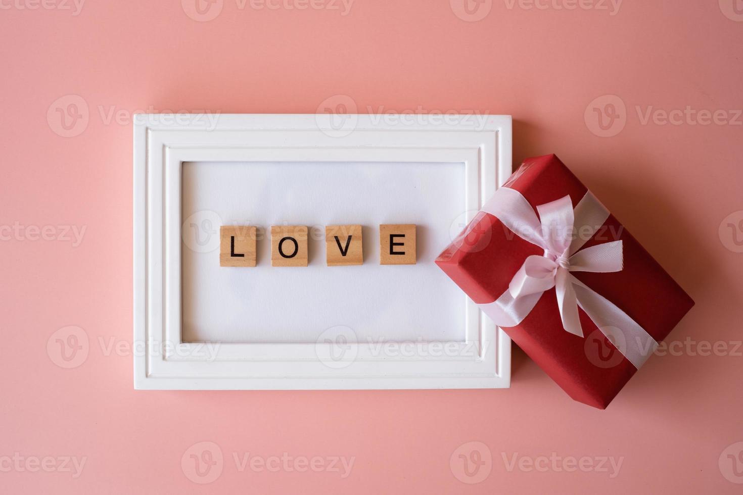 Red gift box and photo frame with letter words of love on pink background for giving in holidays with copy space for text. Holidays, present, giving. New year day, Christmas day, Chinese New Year.