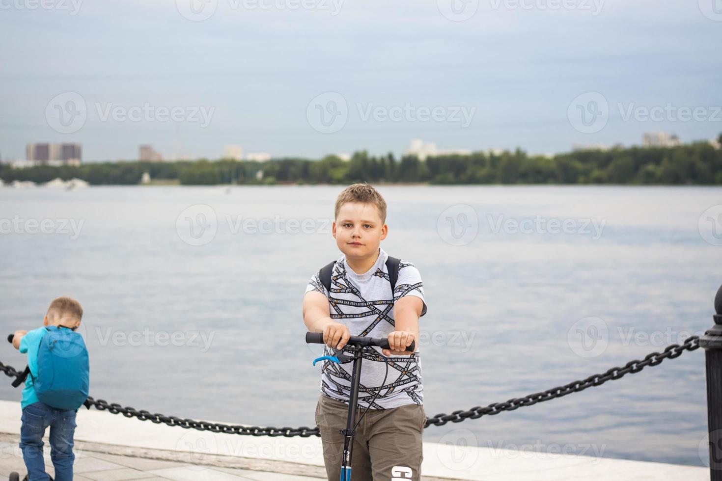 A boy on a scooter along the embankment of the city. Journey. Backpack on the back. The face expresses natural joyful emotions. Not staged photos from life