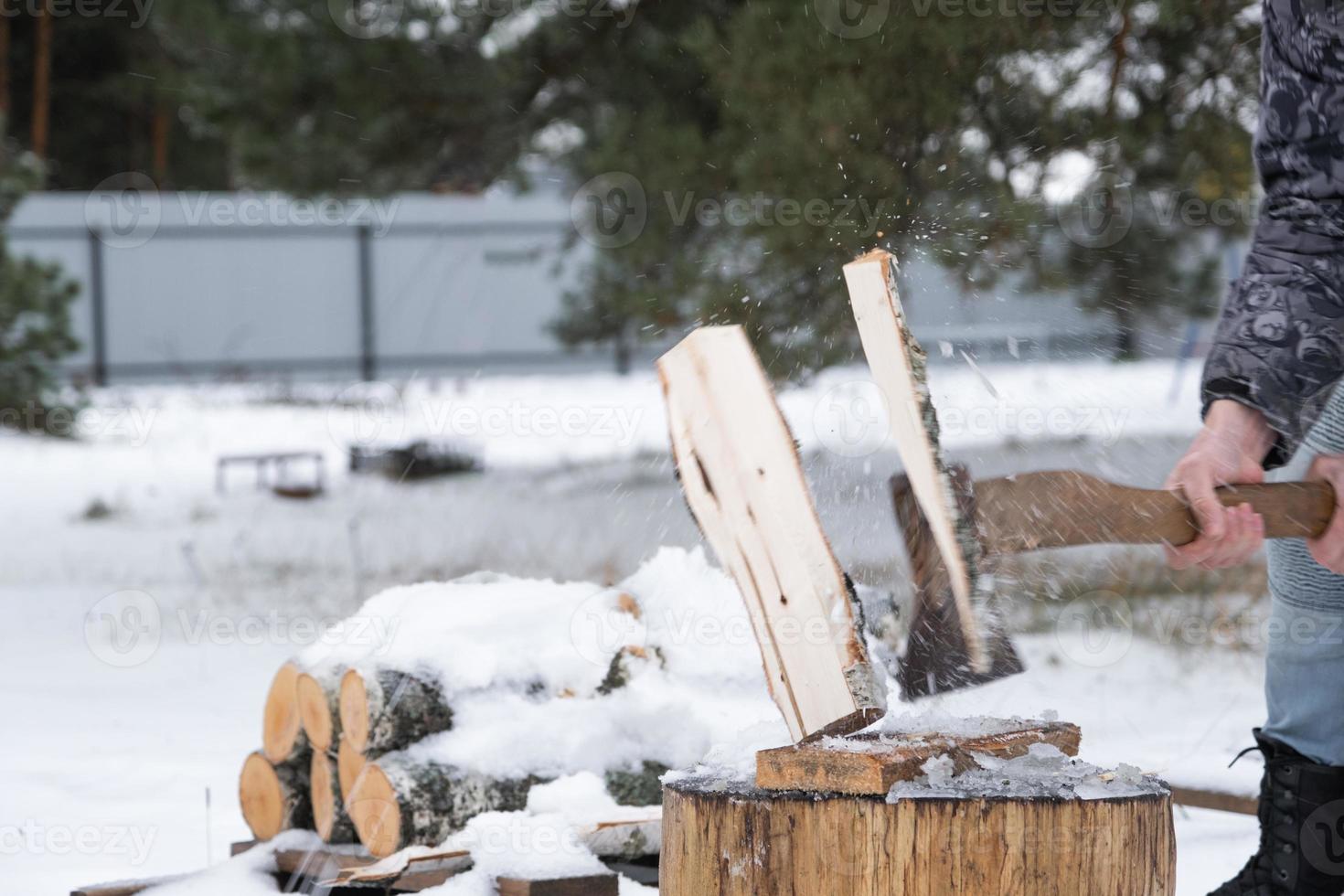 A man is chopping firewood with an axe in winter outdoor in the snow. Alternative heating, wood harvesting, energy crisis photo