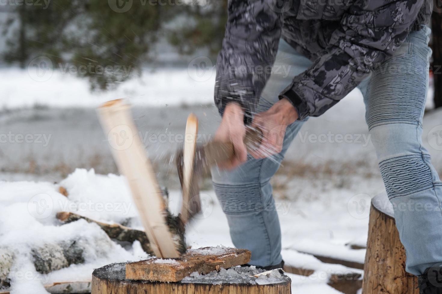 A man is chopping firewood with an axe in winter outdoor in the snow. Alternative heating, wood harvesting, energy crisis photo