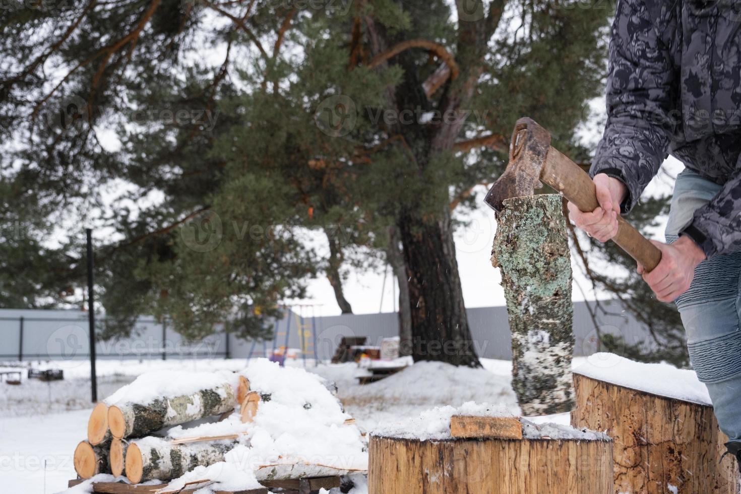 A man is chopping firewood with an axe in winter outdoor in the snow. Alternative heating, wood harvesting, energy crisis photo