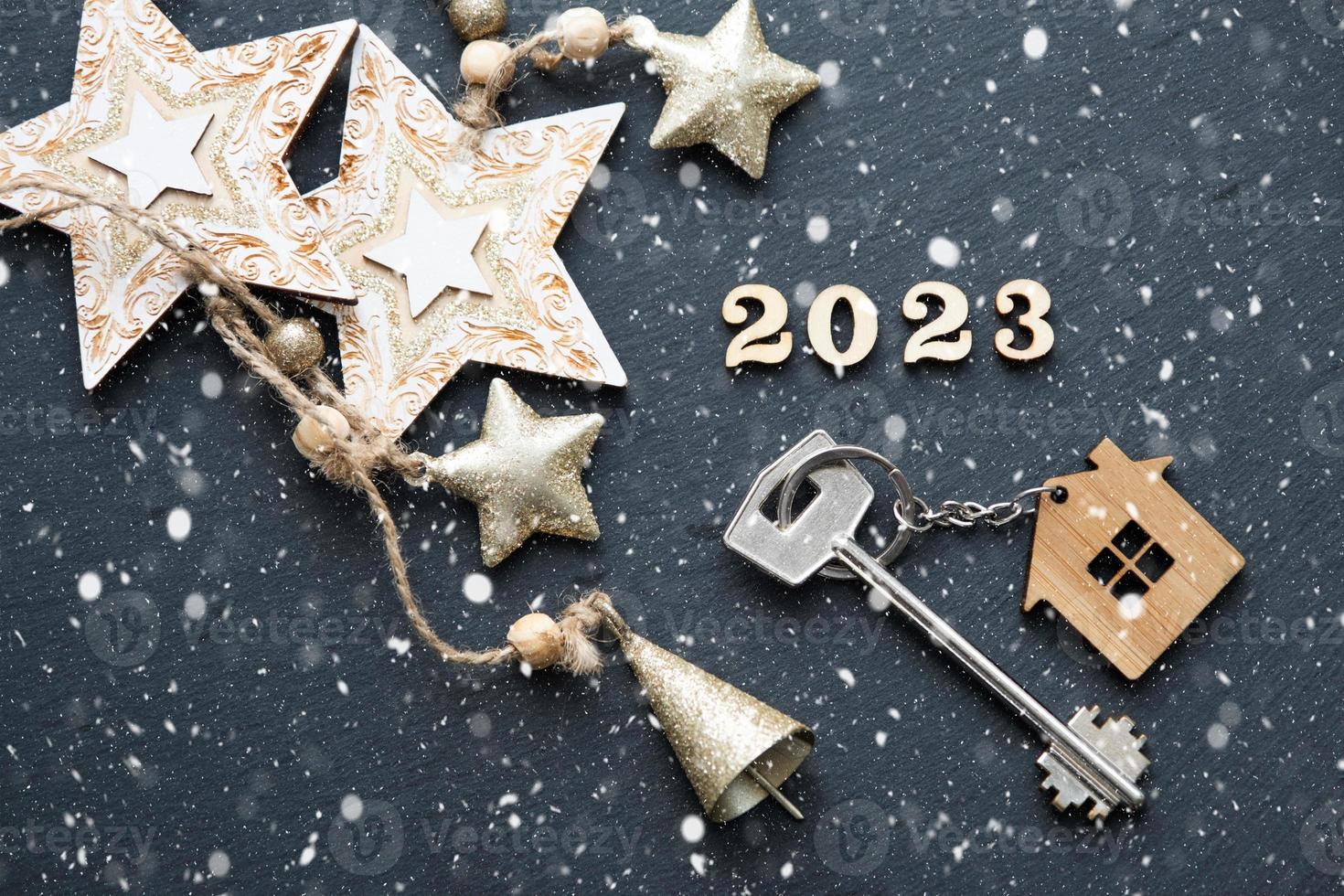 llave de casa con casa de llavero sobre fondo negro con estrellas, copos de nieve. feliz año nuevo 2023-letras de madera, tarjeta de felicitación. compra, construcción, reubicación, hipoteca foto