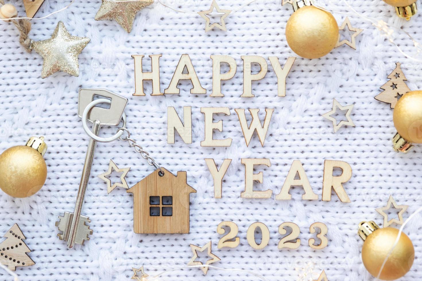 llave de casa con cabaña de llavero sobre fondo de punto festivo con estrellas, luces de guirnaldas. feliz año nuevo 2023-letras de madera, tarjeta de felicitación. compra, construcción, reubicación, hipoteca foto