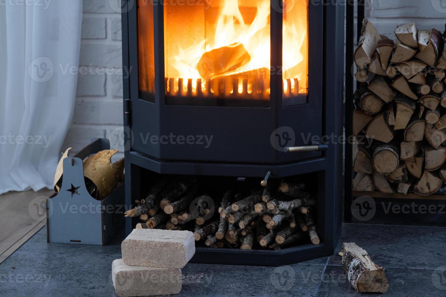 Fuel briquettes made of pressed sawdust for kindling the furnace - economical alternative eco-friendly fuel for the fireplace in the house. Firewood is burning in the oven in the interior photo