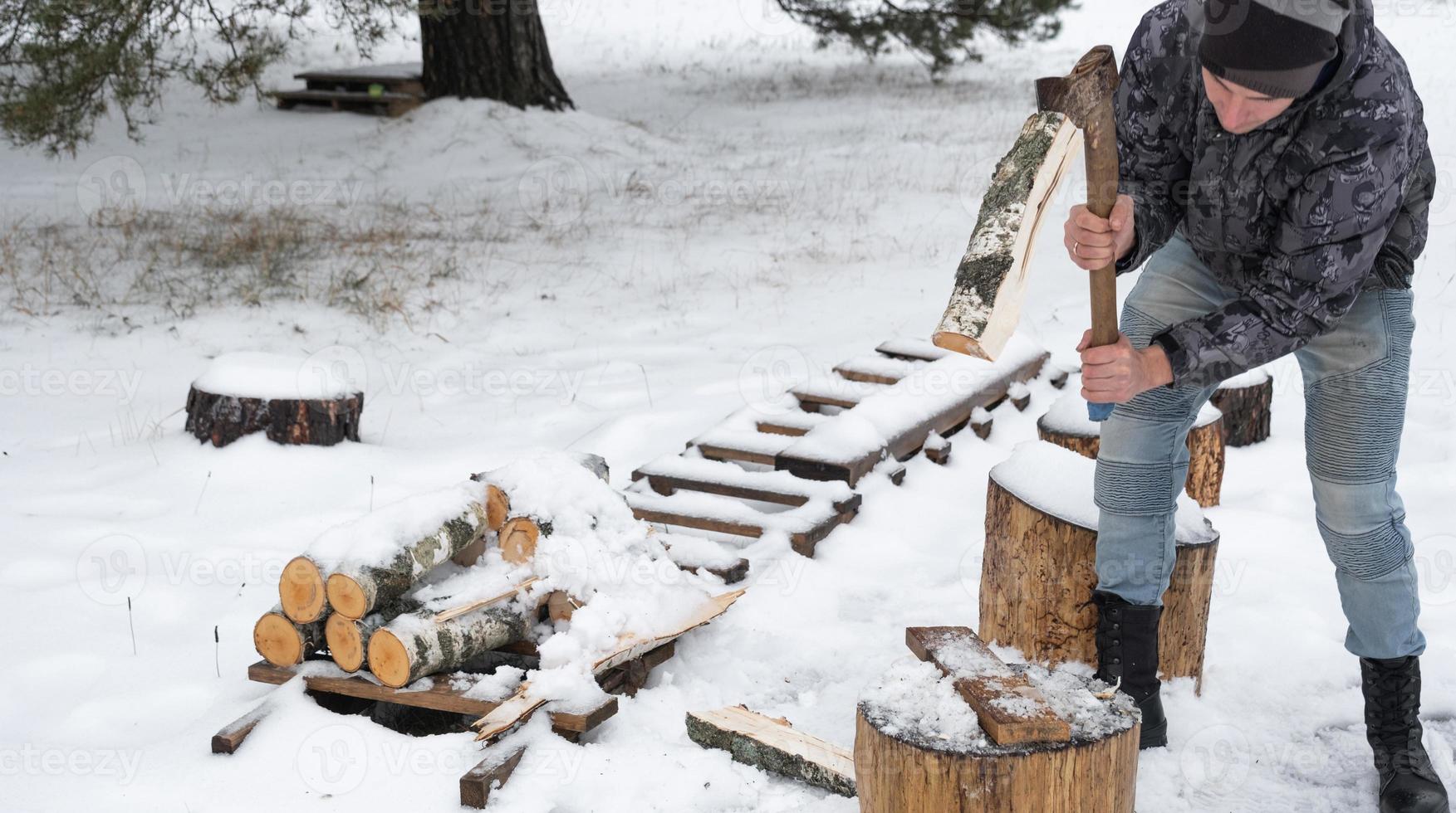 A man is chopping firewood with an axe in winter outdoor in the snow. Alternative heating, wood harvesting, energy crisis photo