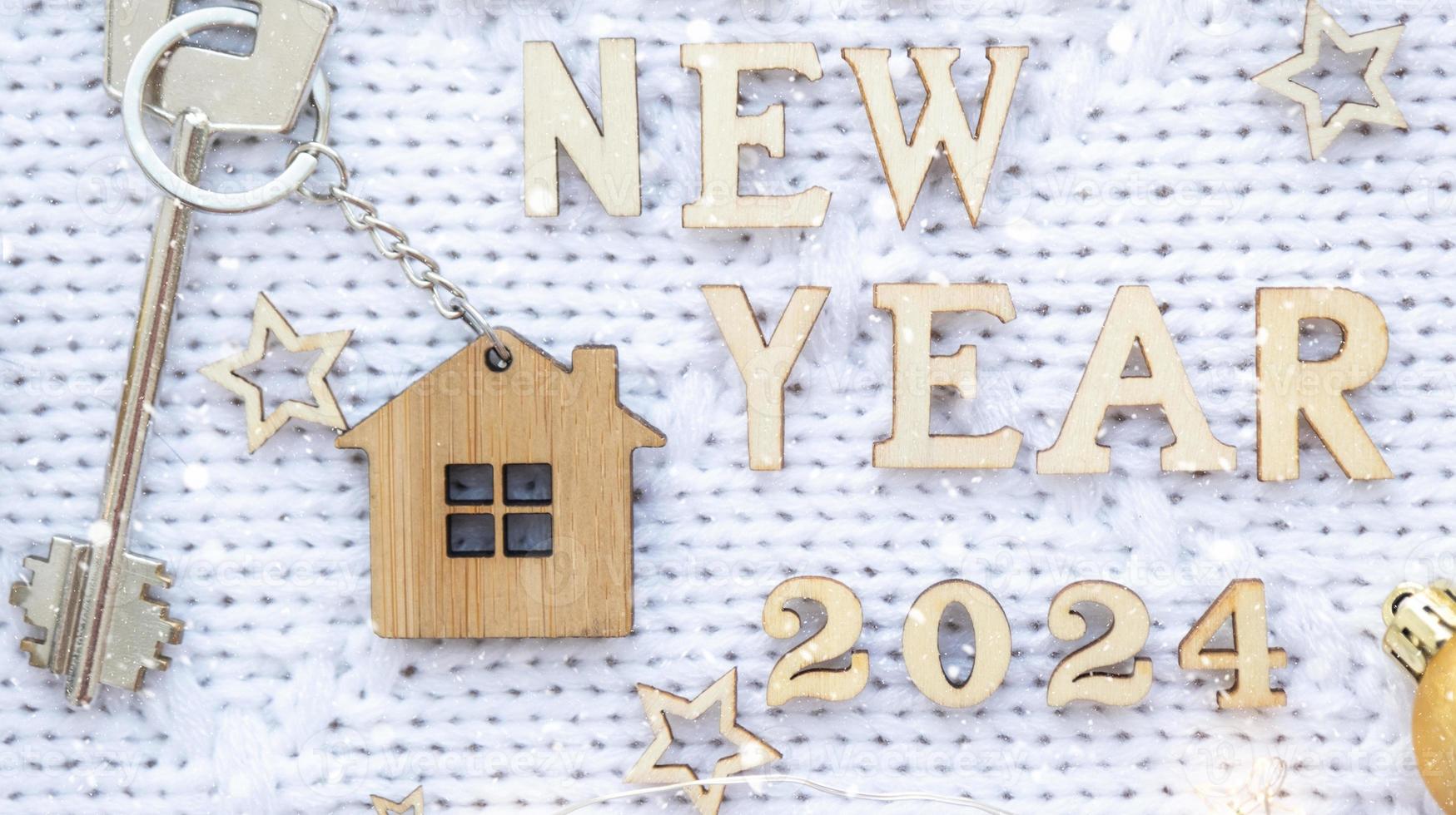 House key with keychain cottage on festive knitted background with stars, lights of garlands. Happy New Year 2024-wooden letters, greeting card. Purchase, construction, relocation, mortgage photo