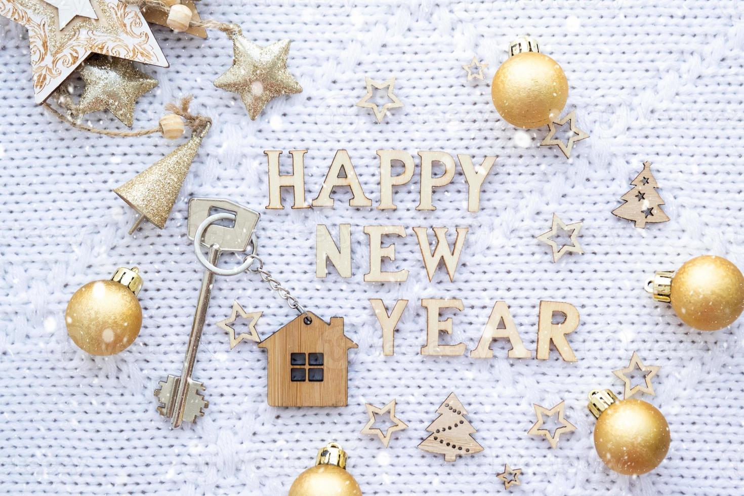 House key with keychain cottage on a festive knitted background with sequins, stars, lights of garlands. Happy New Year-wooden letters, greeting card. Purchase, construction, relocation, mortgage photo