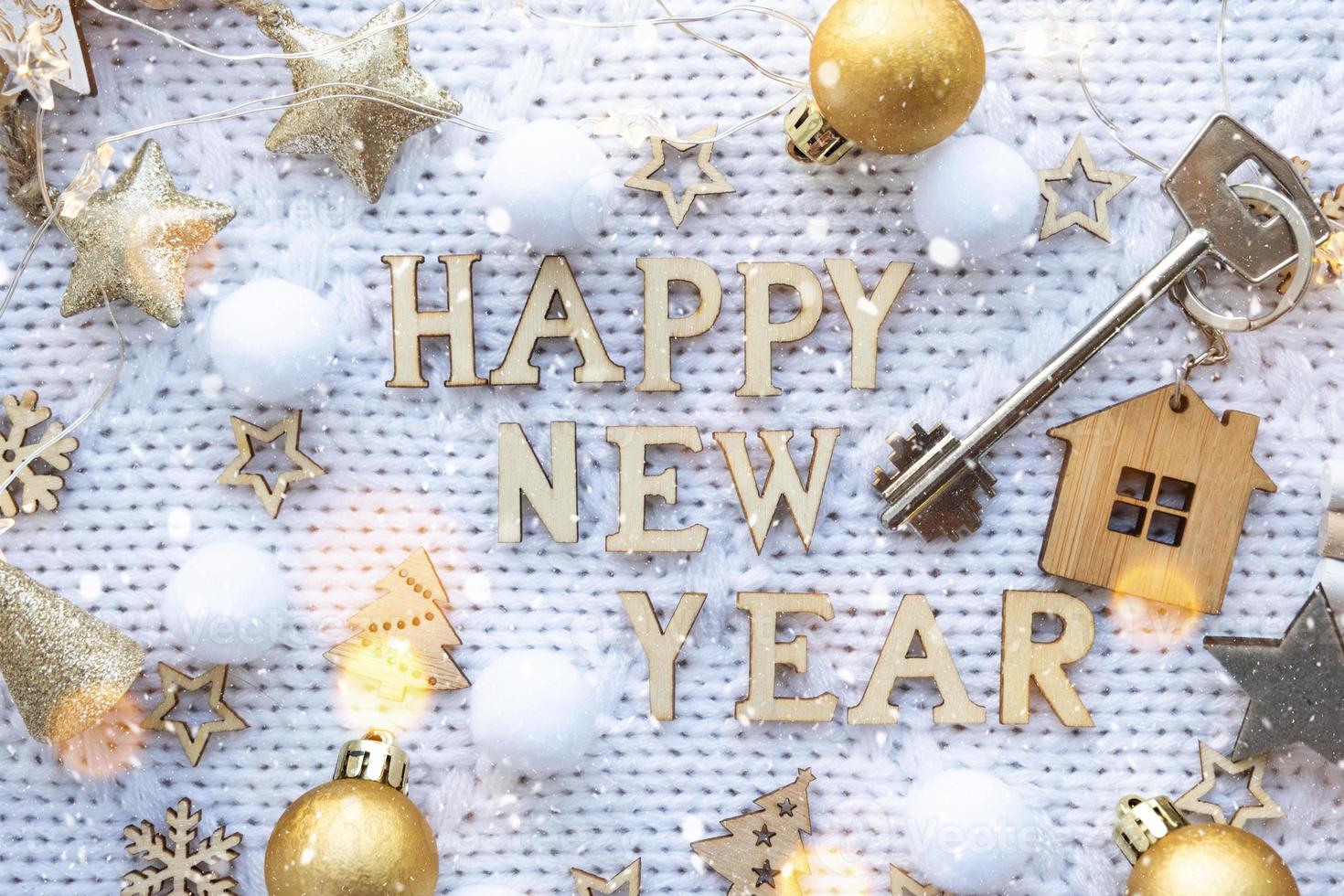 House key with keychain cottage on a festive knitted background with sequins, stars, lights of garlands. Happy New Year-wooden letters, greeting card. Purchase, construction, relocation, mortgage photo